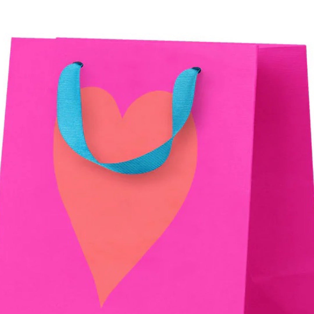 Pink gift bag with a heart design and blue handle on a white background.