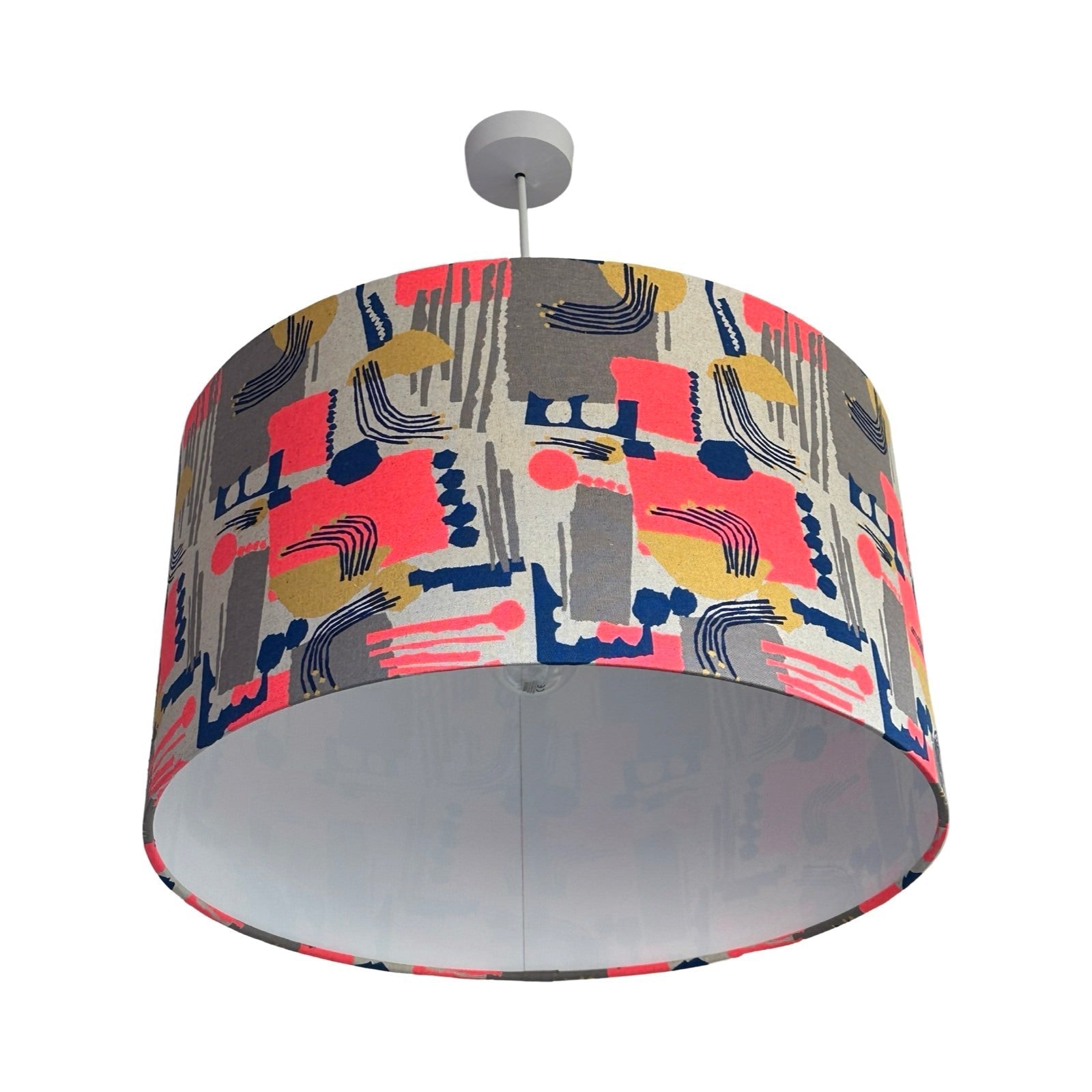 Drum lampshade covered in cotton/linen blend fabric with an abstract shapes pattern in neon pink, navy, gold and grey.