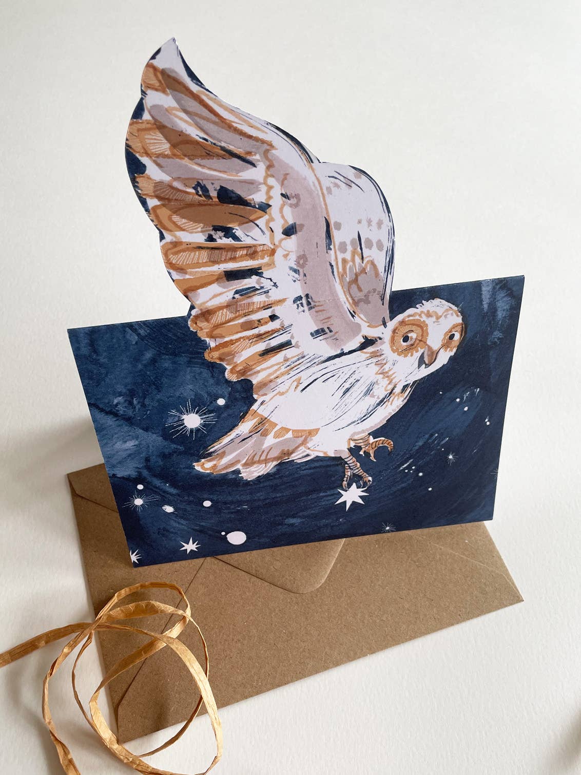 Greeting card with a owl design on a starry night background, accompanied by a brown envelope and gold ribbon.