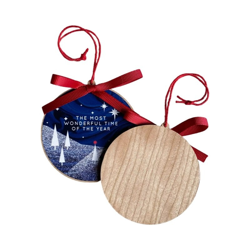 Circular Christmas decoration featuring an illustration of a wooden lodge in a forest under the northern lights and the text 'the most wonderful time of the year'.