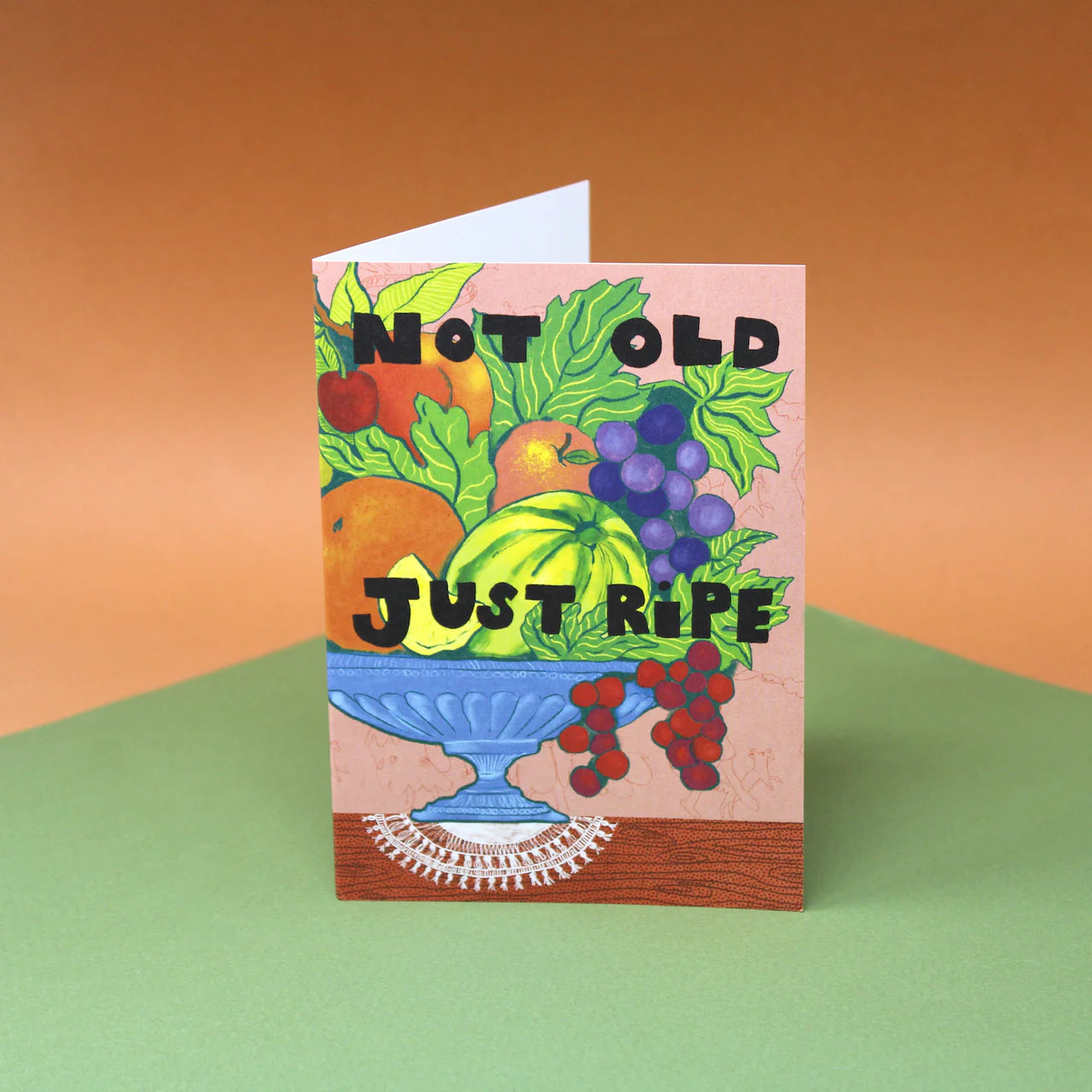 Greeting card with fruit illustration and 'Not Old Just Ripe' text on an orange and green background.