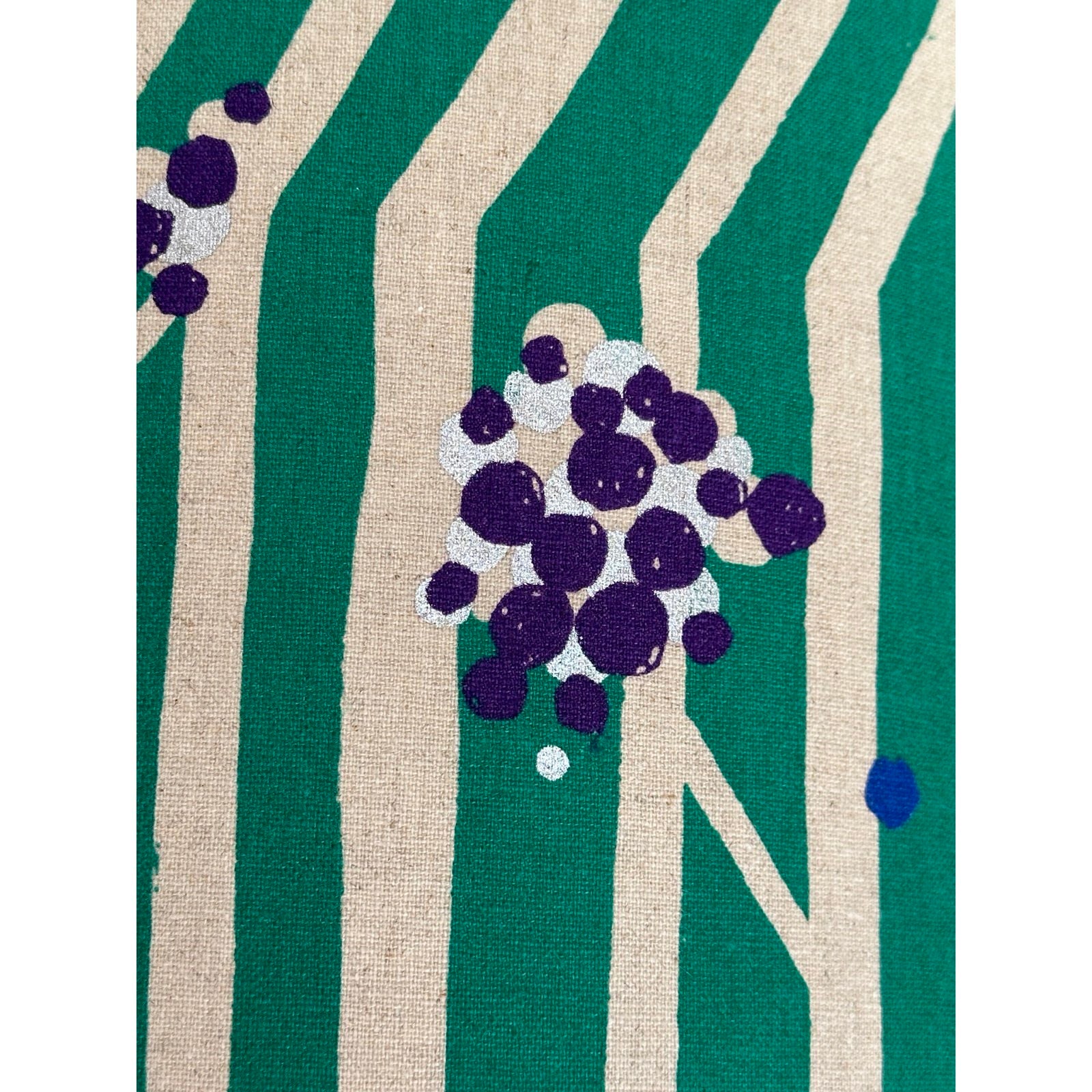 A cushion cover with green and white stripes, featuring white branches with clusters of purple nuts.
