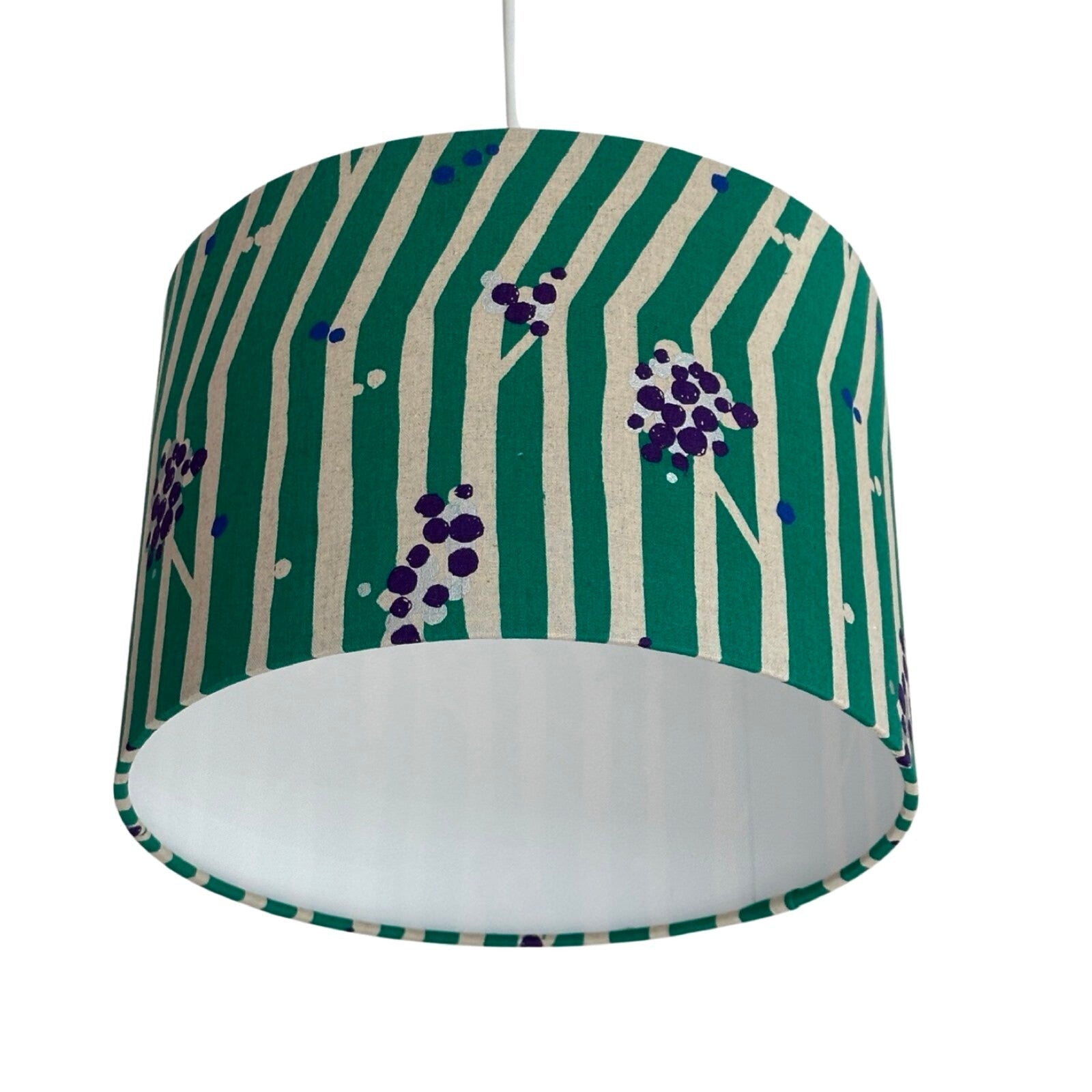 Close up of a drum lampshade featuring purple and silver clusters of nuts and white tree branches against a green background