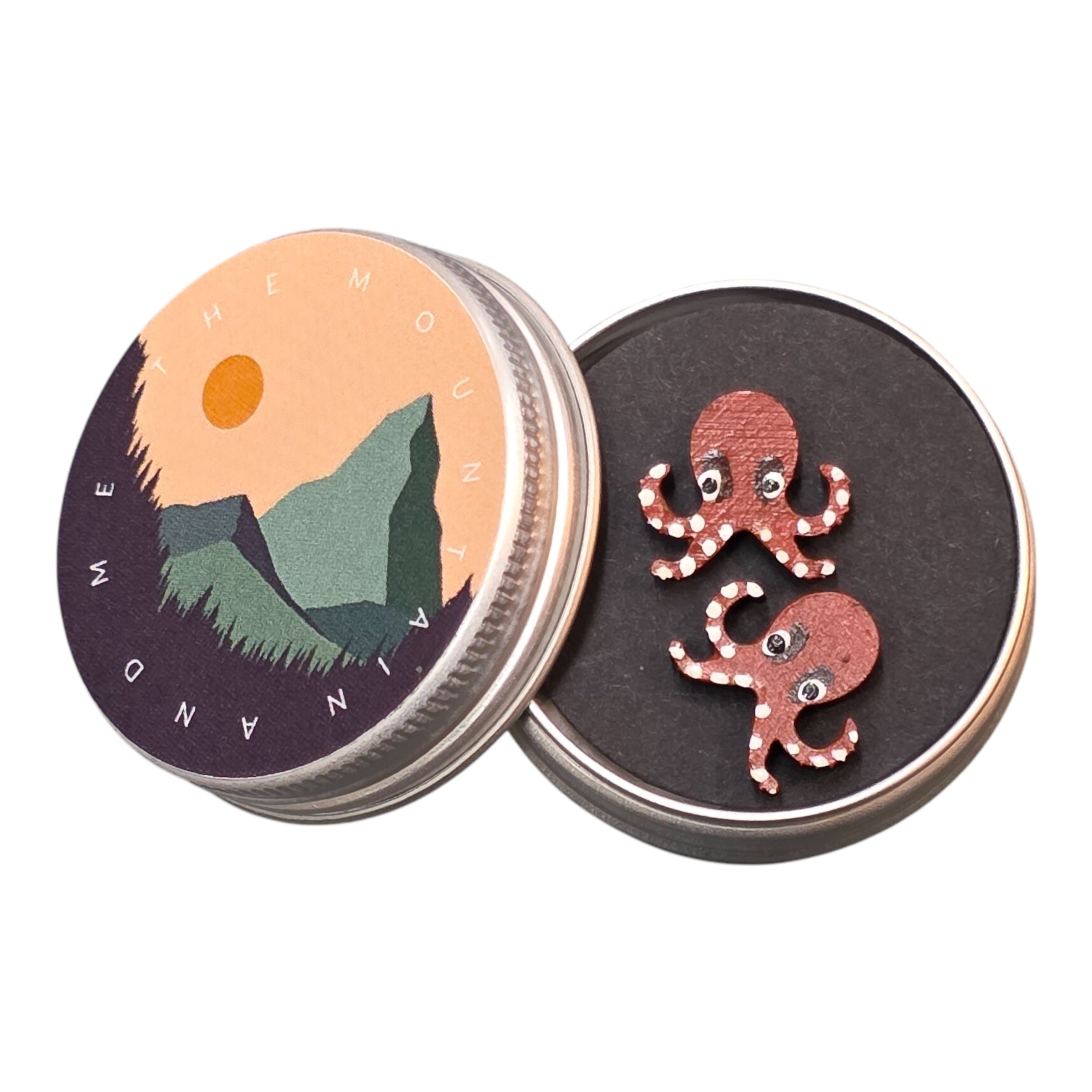 A pair of pink octopus-shaped wooden earrings in a small metal tin.