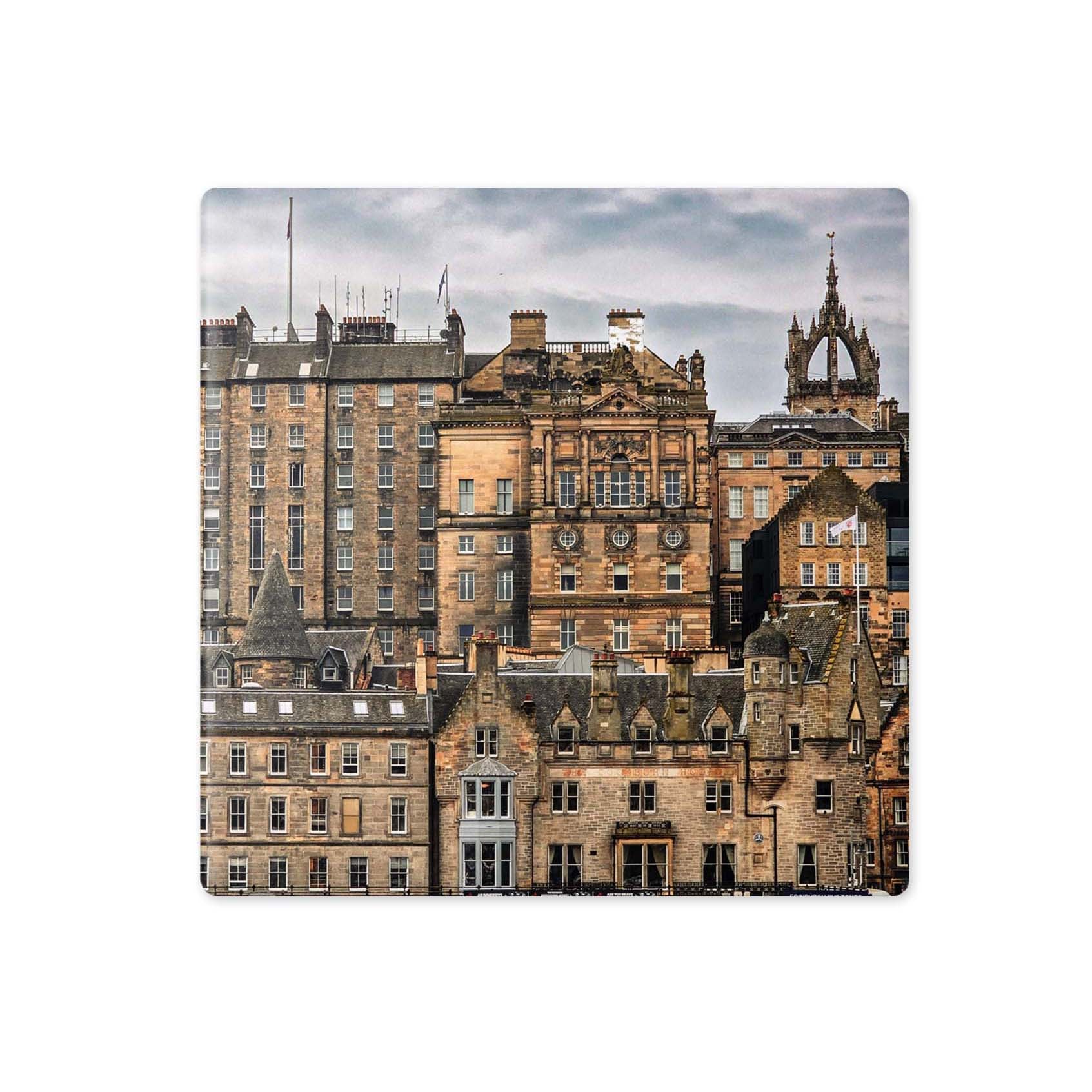 A square coaster featuring a photographic print of historic Edinburgh buildings under a cloudy sky, shown on a plain white background.