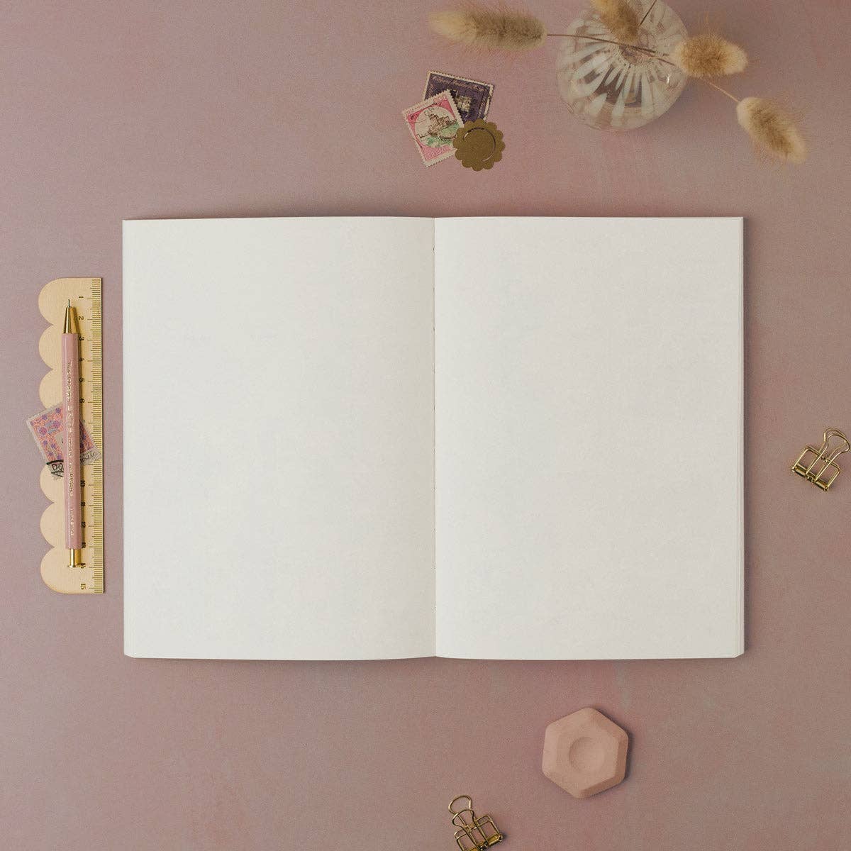 Open notebook on a pink surface with decorative items.