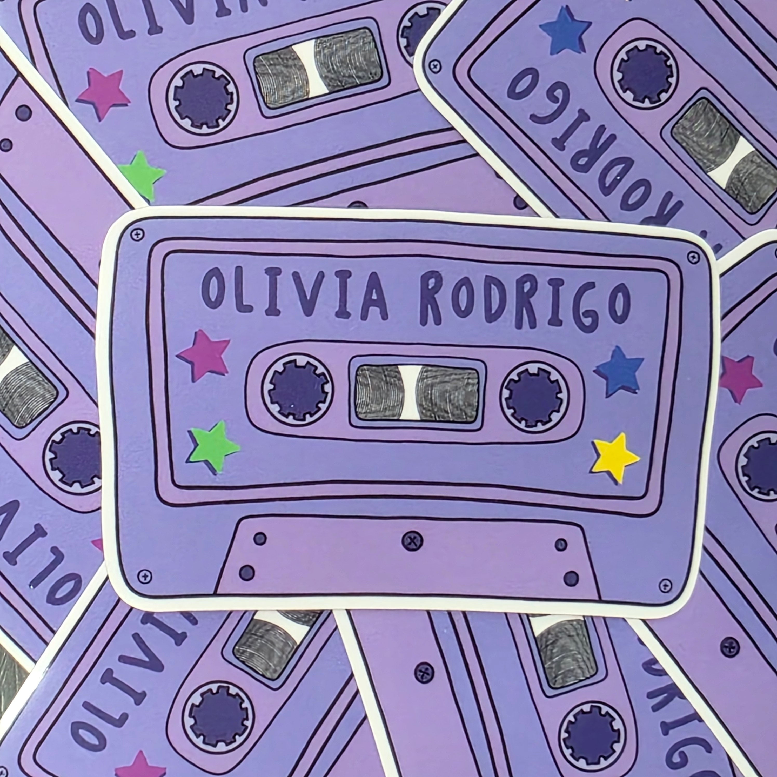 A rectangular-shaped sticker featuring an illustration of a retro cassette tape in dark and light purple with the title 'Olivia Rodrigo', decorated with colourful stars. 