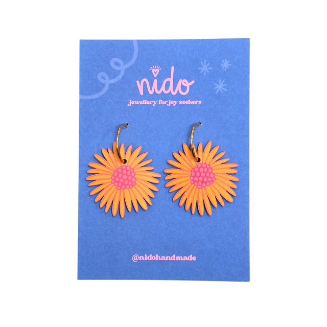 These wooden blossom-shaped earrings feature orange and yellow petals with a pink centre presented on a blue backing card