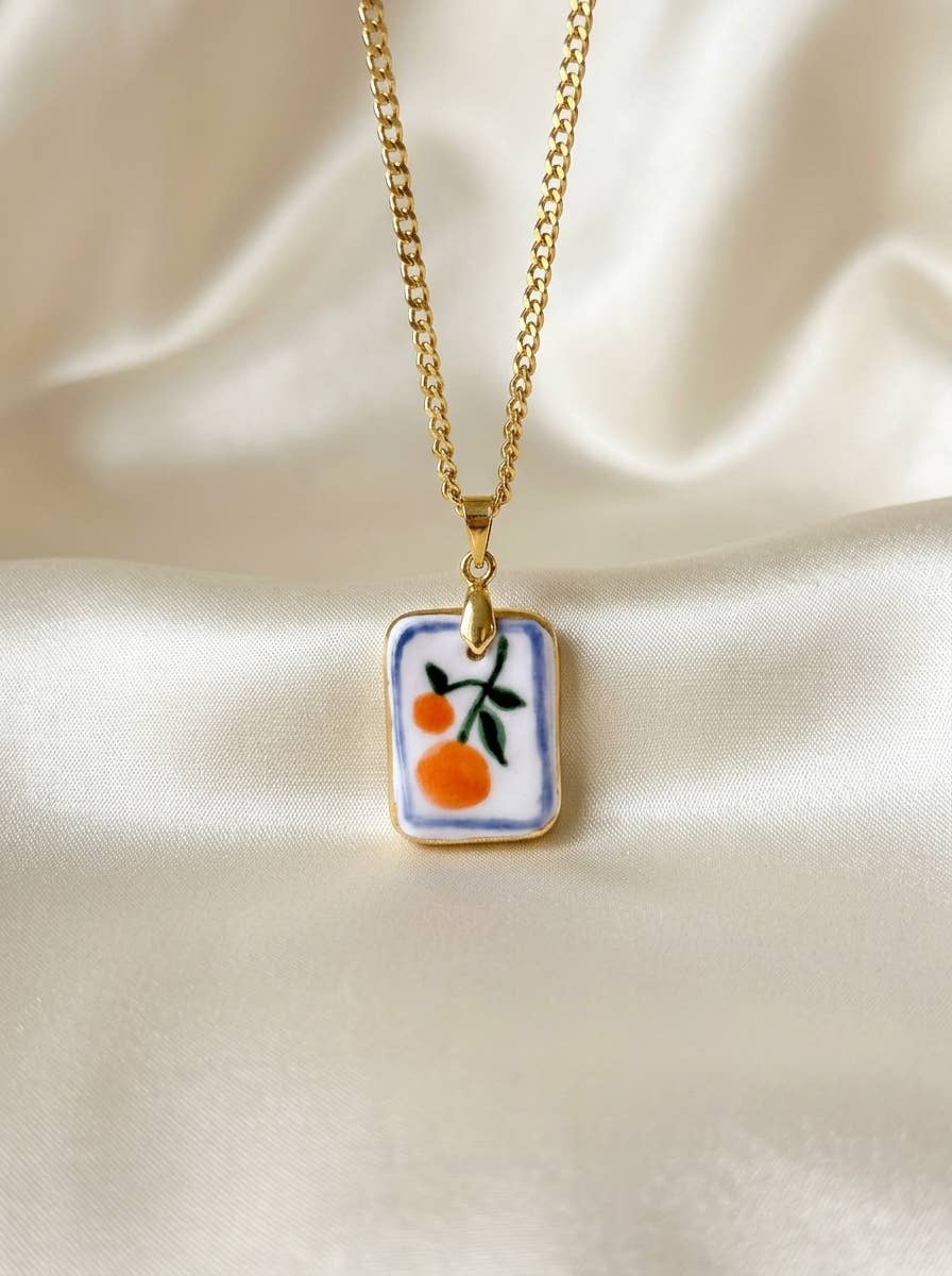 Necklace with a rectangular pendant featuring a design of oranges on a beige fabric background.