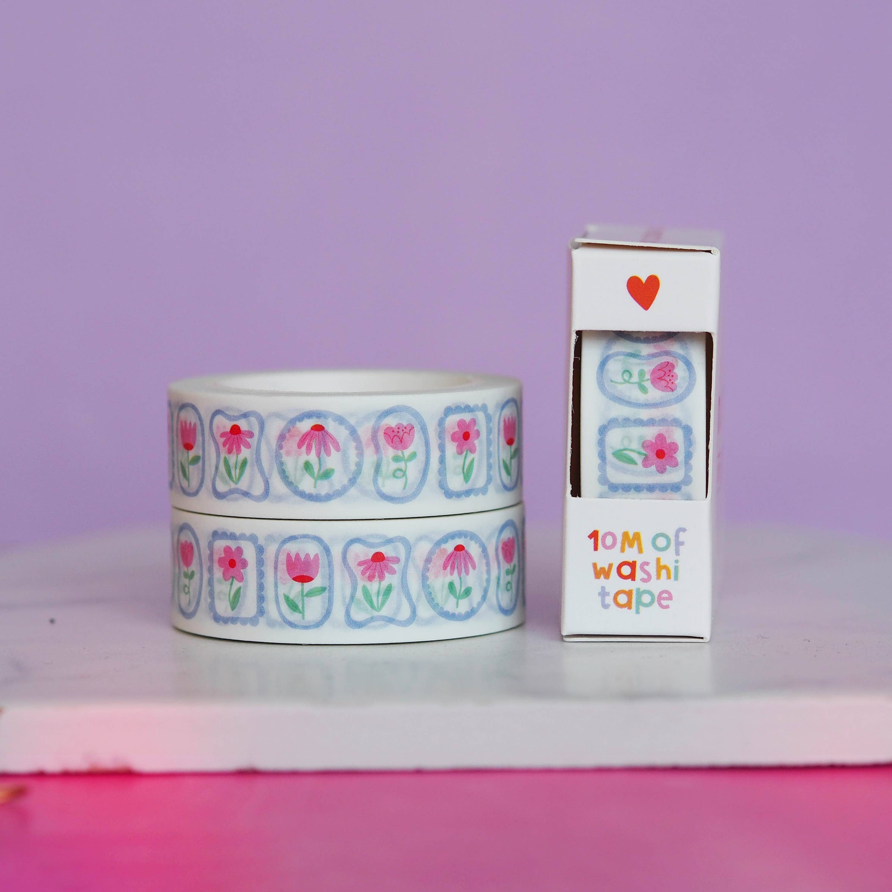 Rolls of washi tape with floral design and packaging on a purple background.