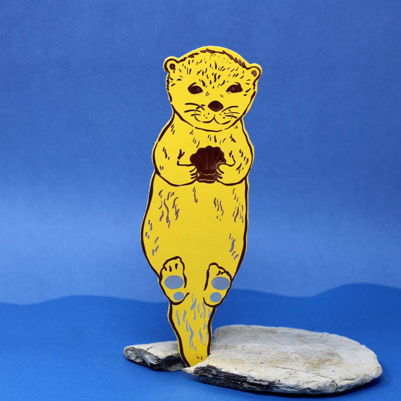 Yellow bear bookmark holding a shell on a blue background.