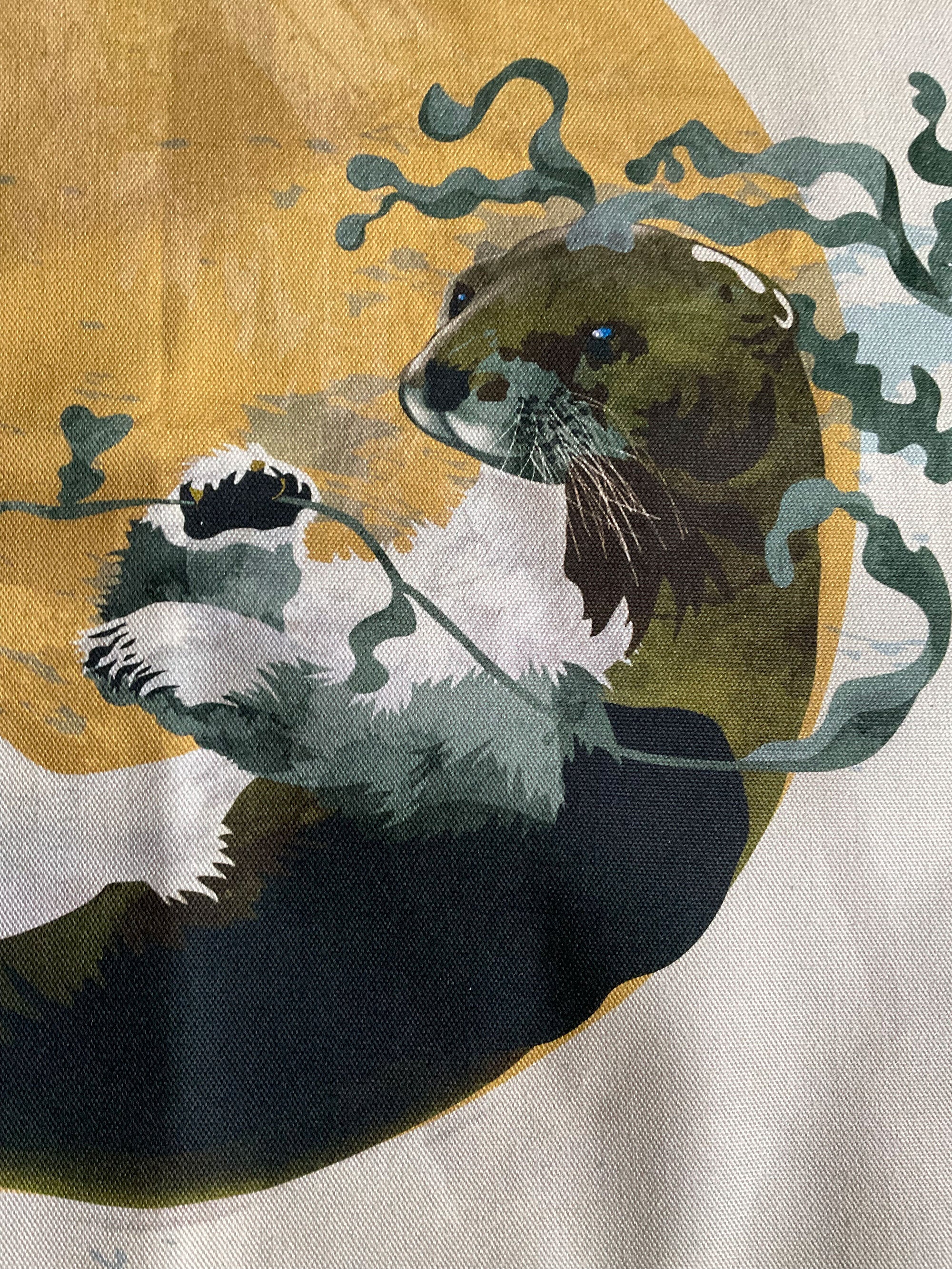 A tea towel featuring an illustration of an otter, in a mustard circle against an off-white background. 