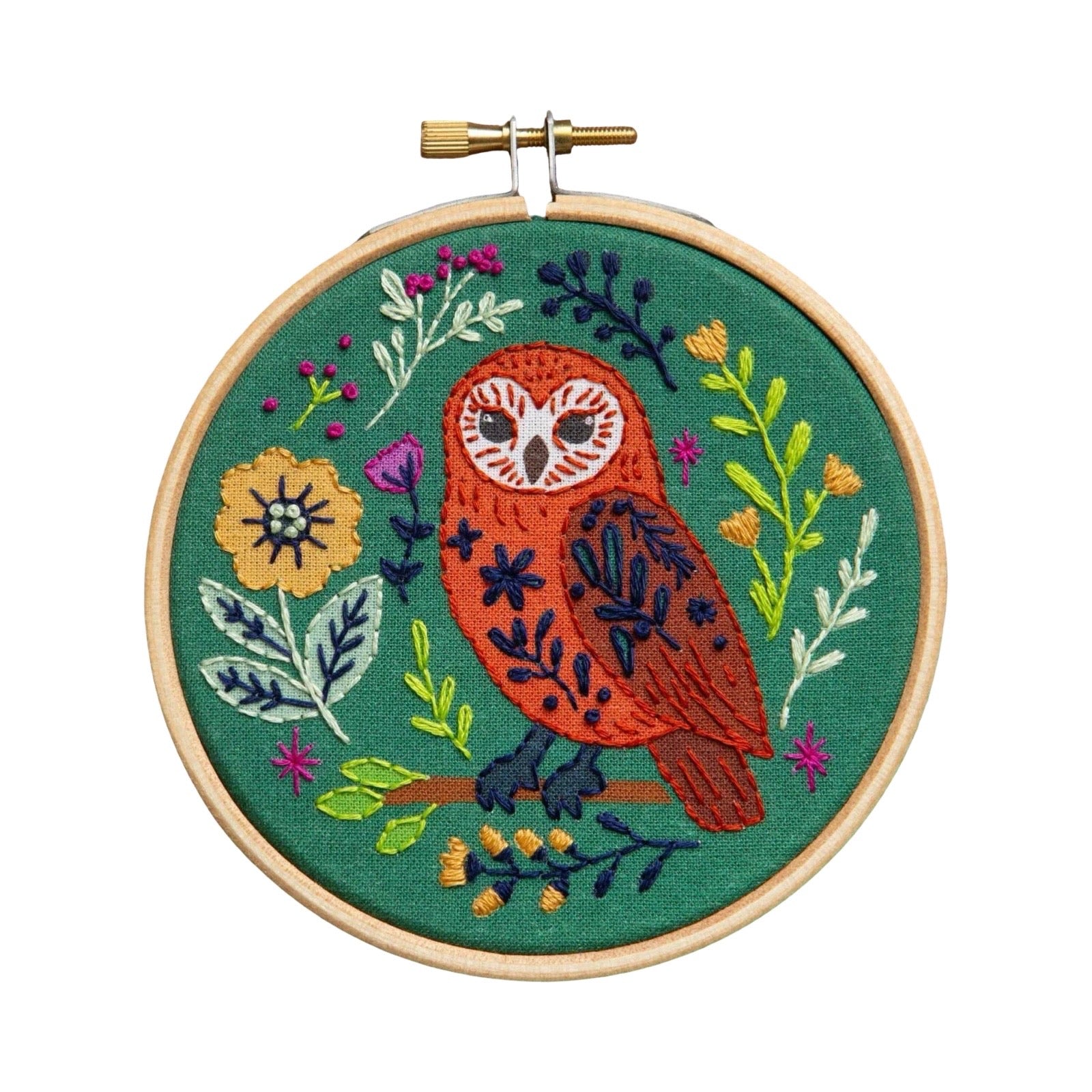 A circular embroidery hoop containing a finished embroidered design of an owl surrounded by flowers and leaves on a green fabric background, photographed against a plain white background.