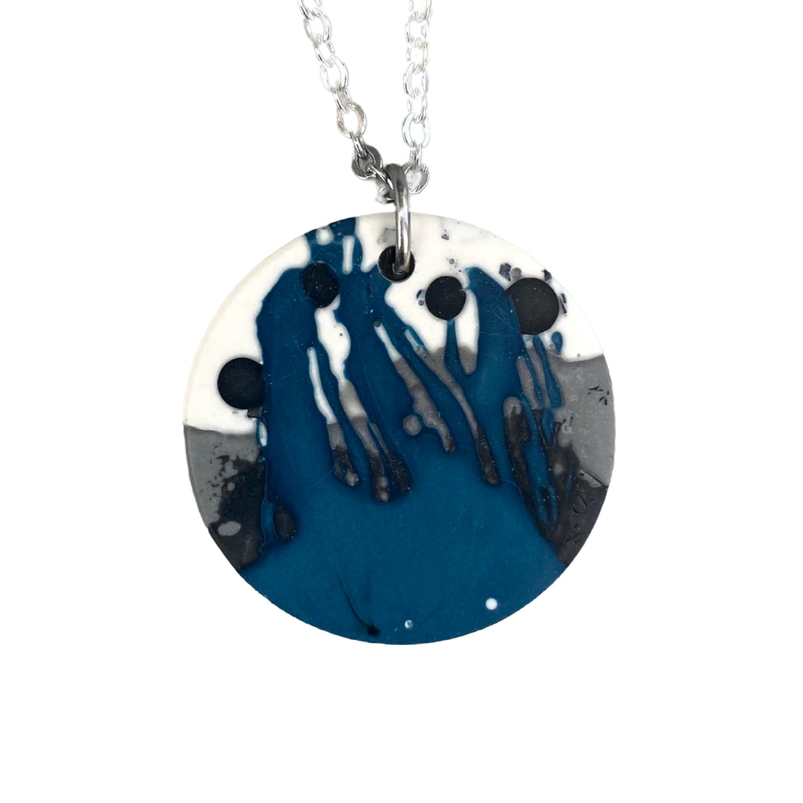 A circular pendant necklace with a blue, black, grey and white design on a silver chain.