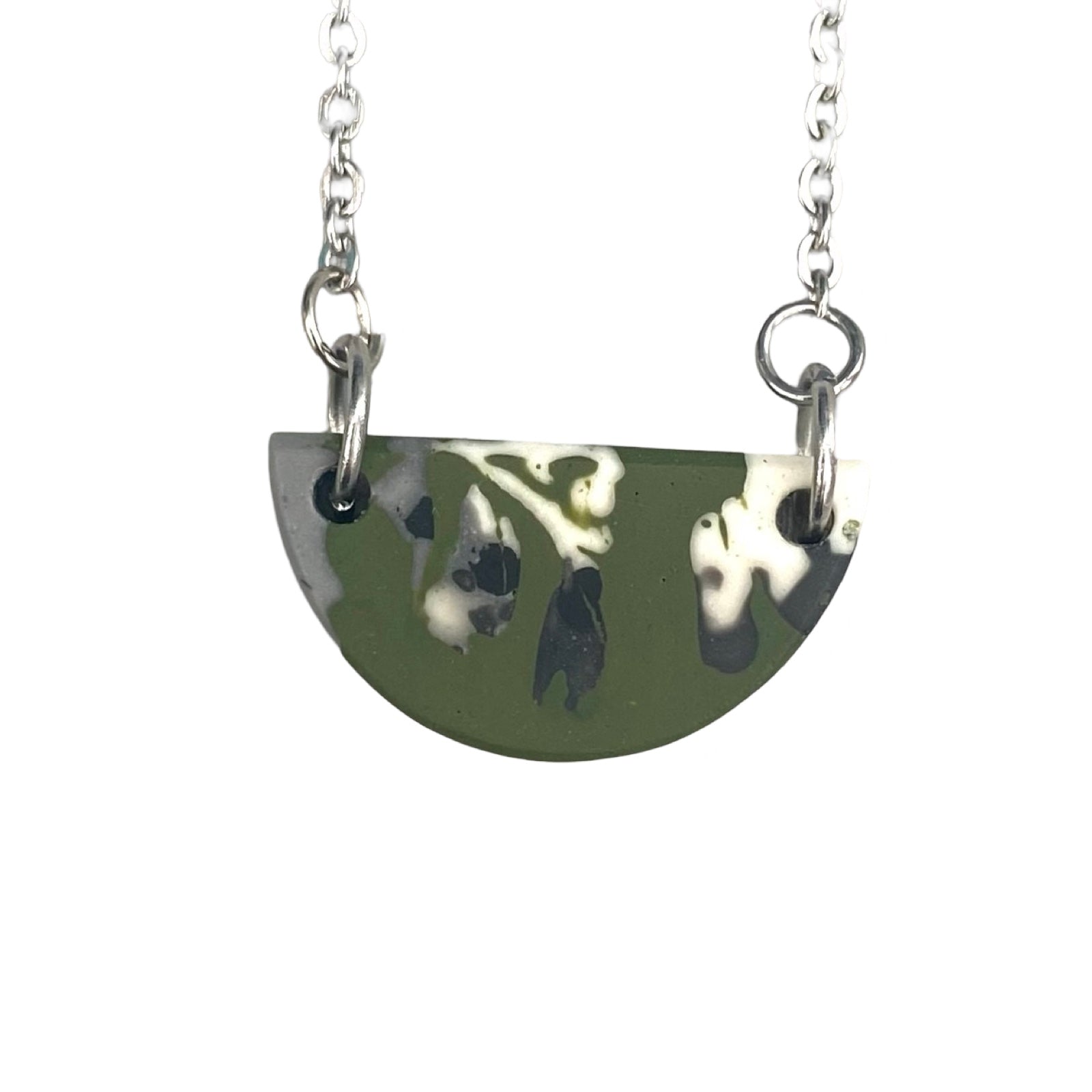 A green half moon necklace with a black and white abstract design on a silver chain.