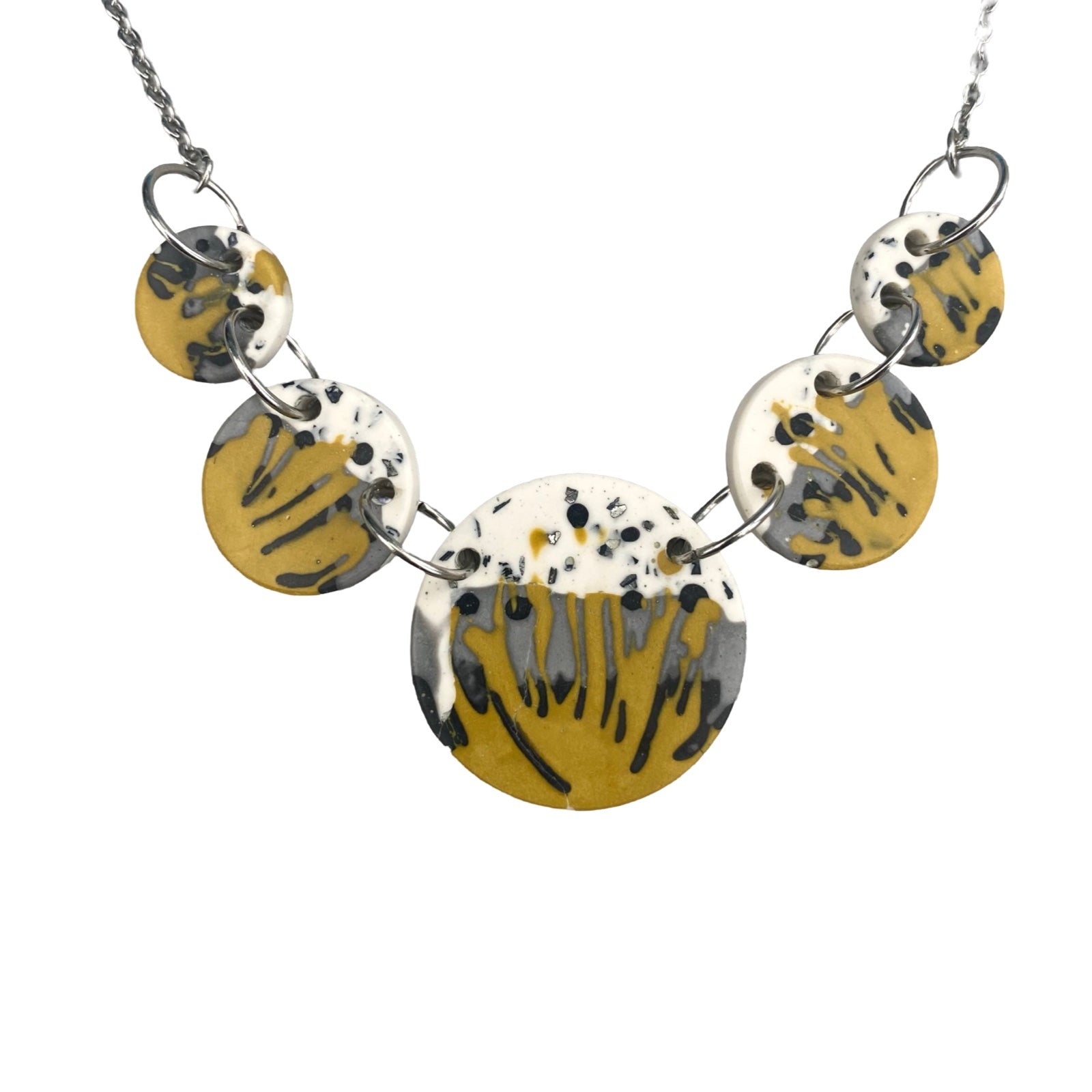 Necklace with 5 mustard circular pendants with a black, grey and white paint design held together with silver findings.