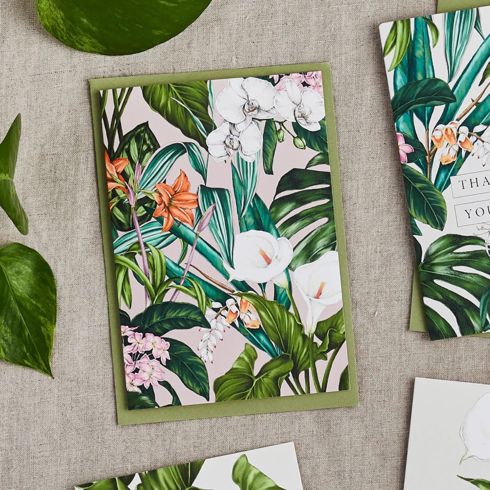 Floral and leaf patterned cards on a textured surface with green leaves.