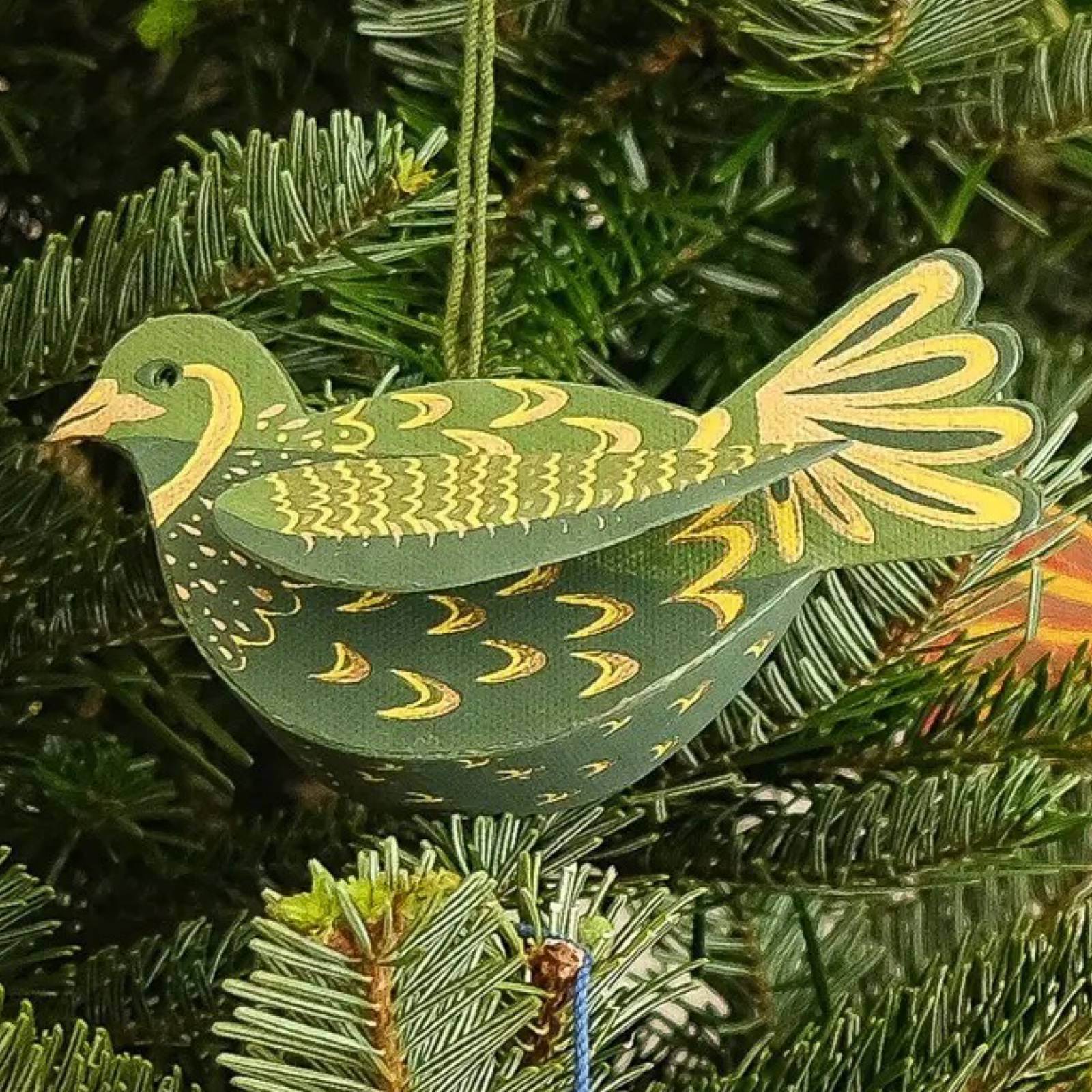 Green cardboard partridge Christmas decoration hanging on a Christmas tree.
