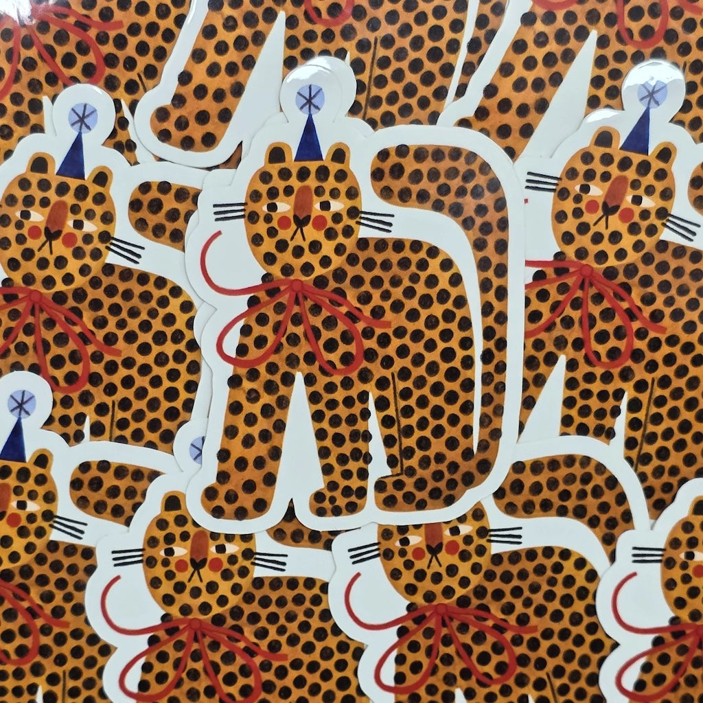 Vinyl sticker of a spotty tiger wearing a big red bow and a blue party hat.