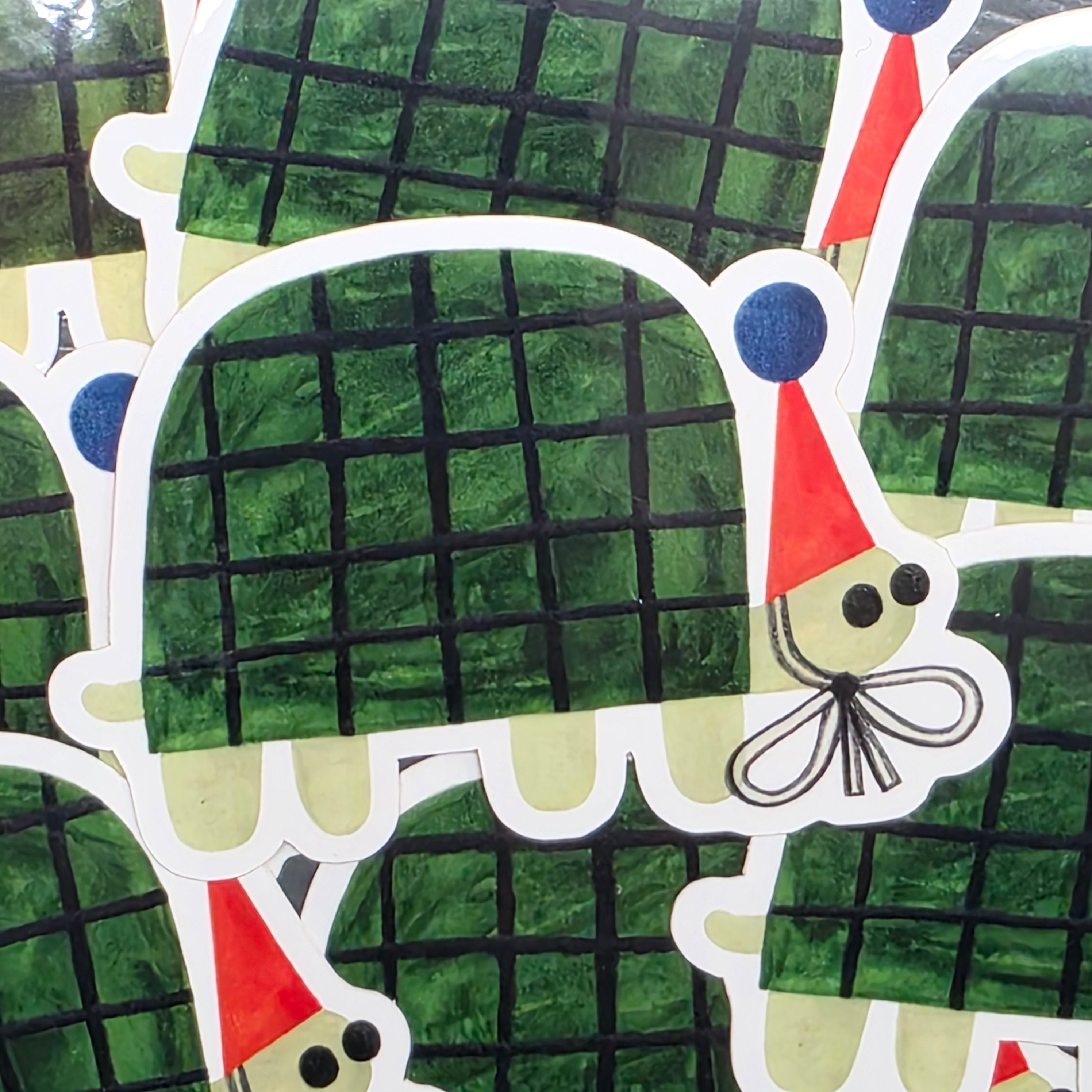 Vinyl sticker of a green turtle wearing a red party hat with a blue pom pom.