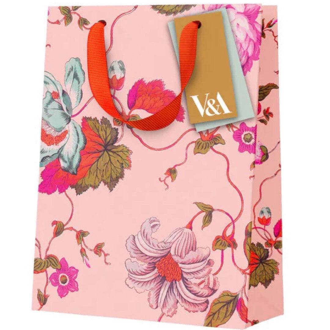 Colourful gift bag featuring pink, white and red flowers against a peach background and a red ribbon handle.