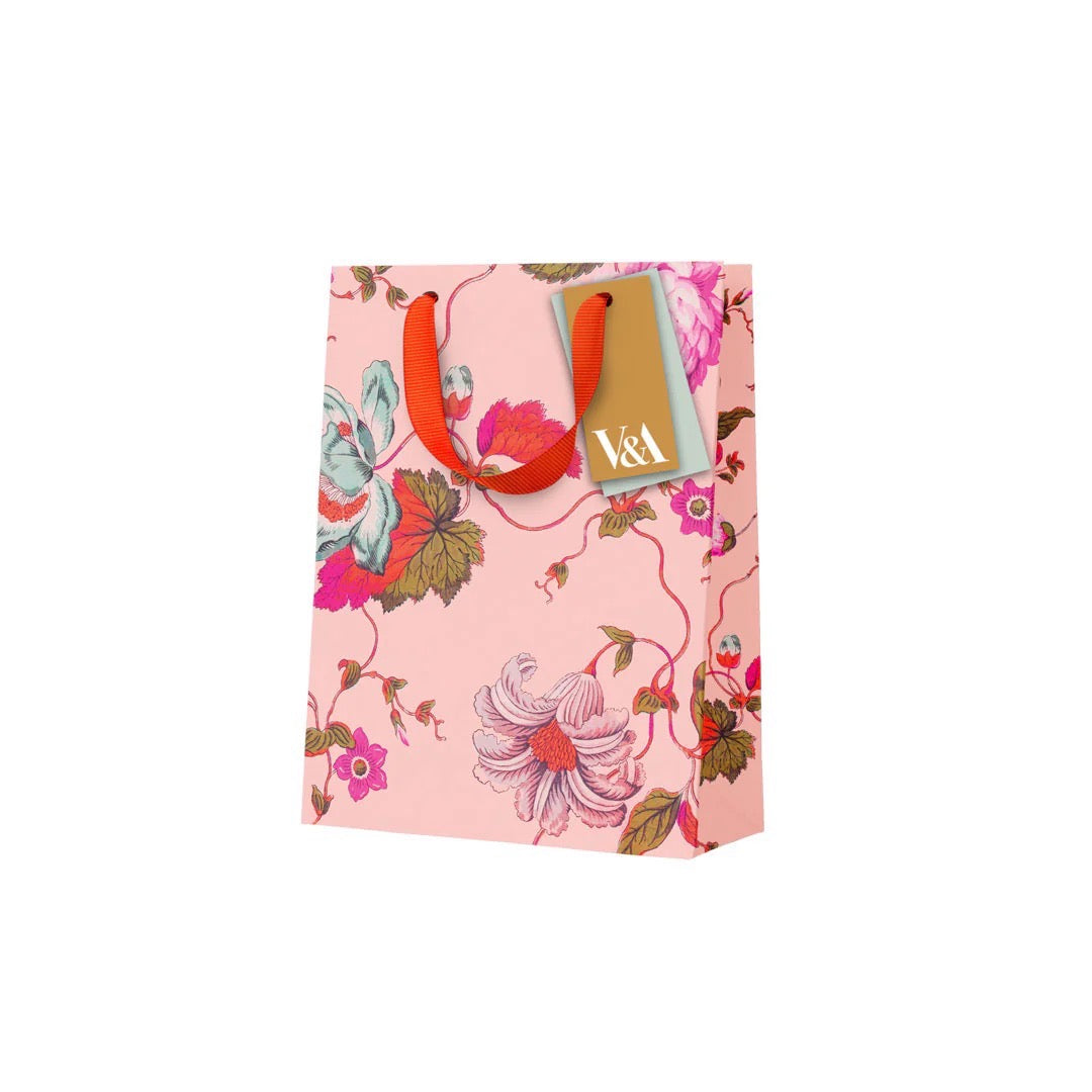 Colourful gift bag featuring pink, white and red flowers against a peach background and a red ribbon handle.