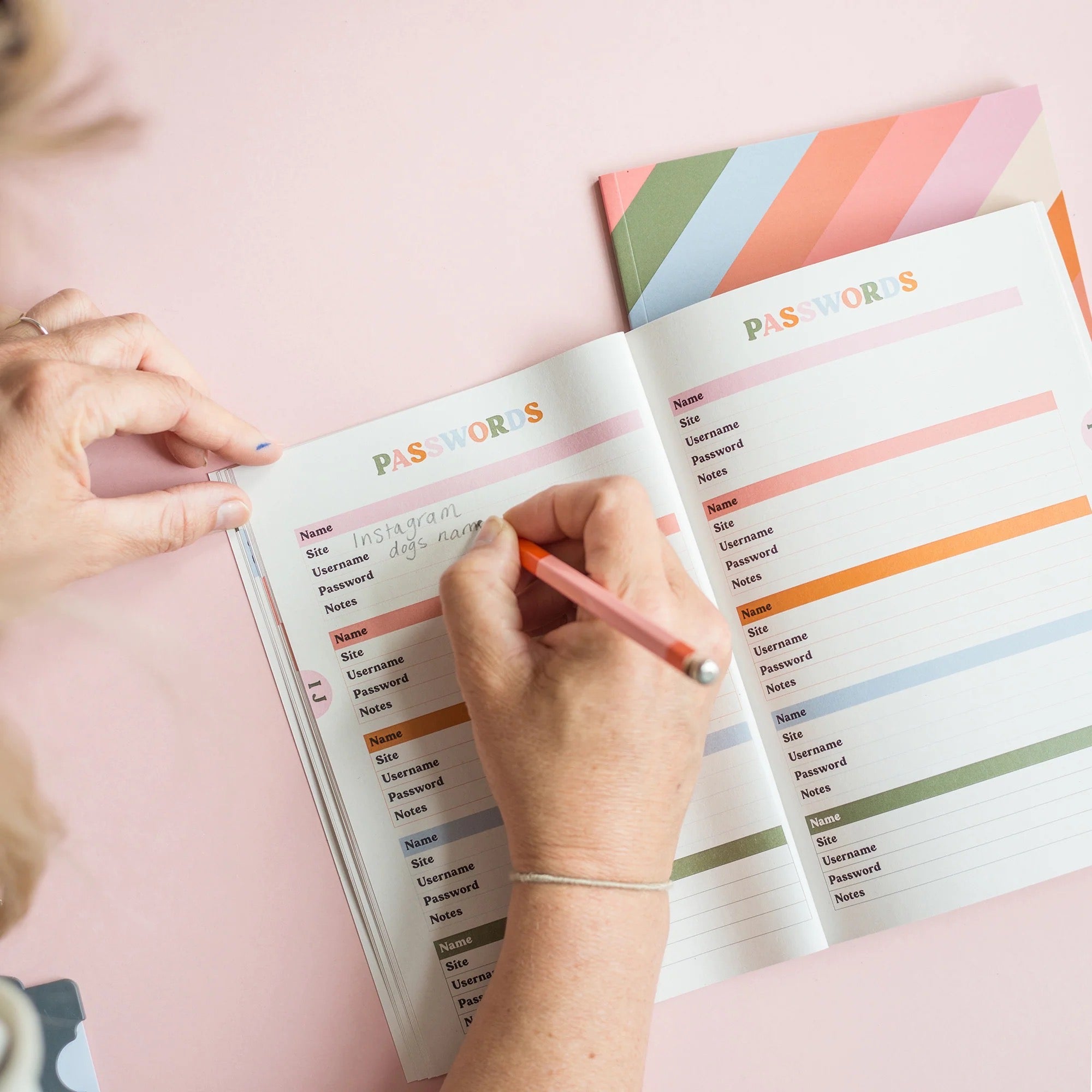 Person using a colourful password manager notebook on a pink surface.
