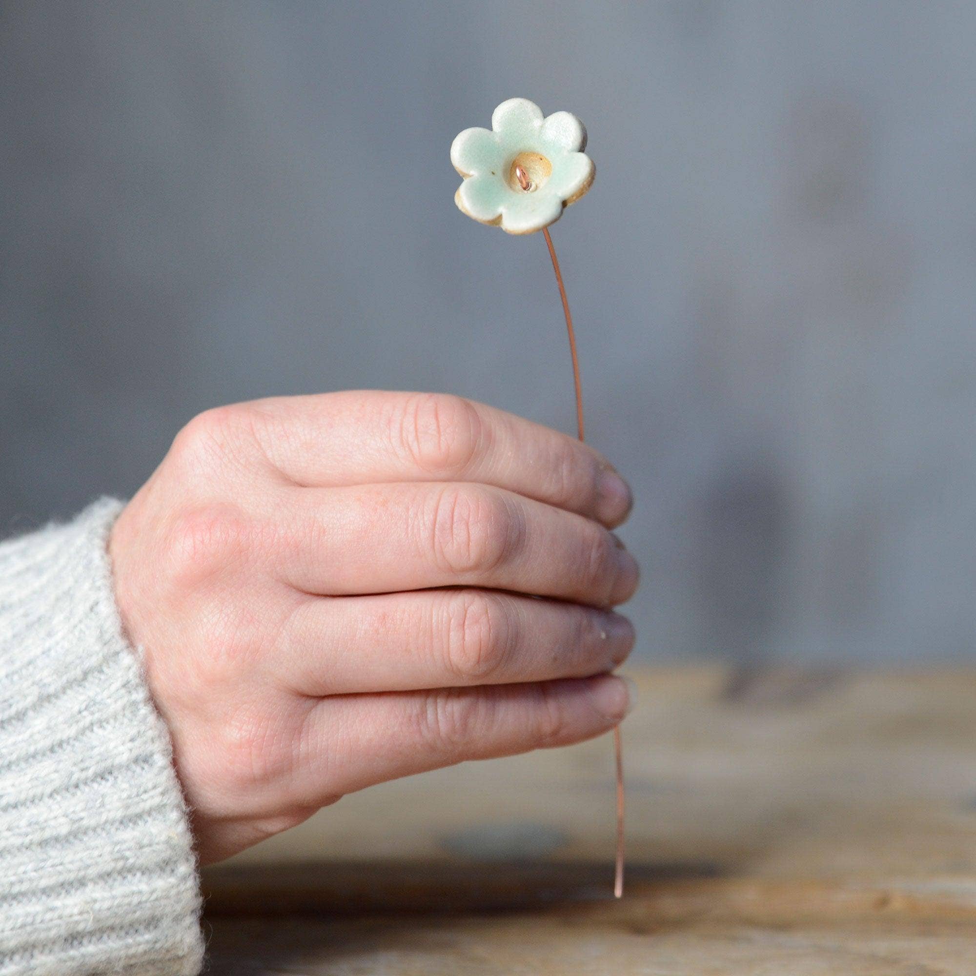 A hand holding a pastel green ceramic flower bud stem on a copper wire