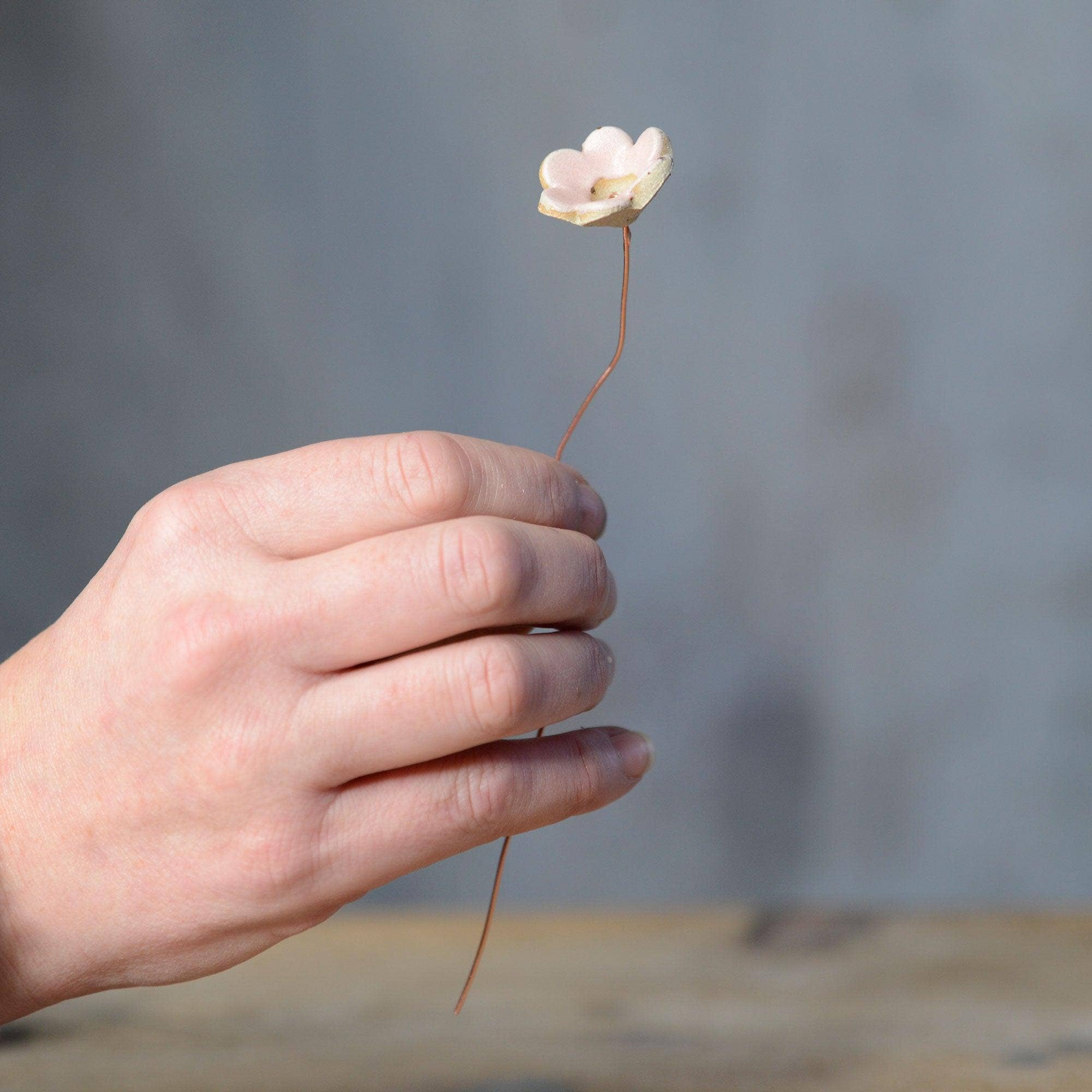 A hand holding a pink ceramic flower bud stem on a copper wire