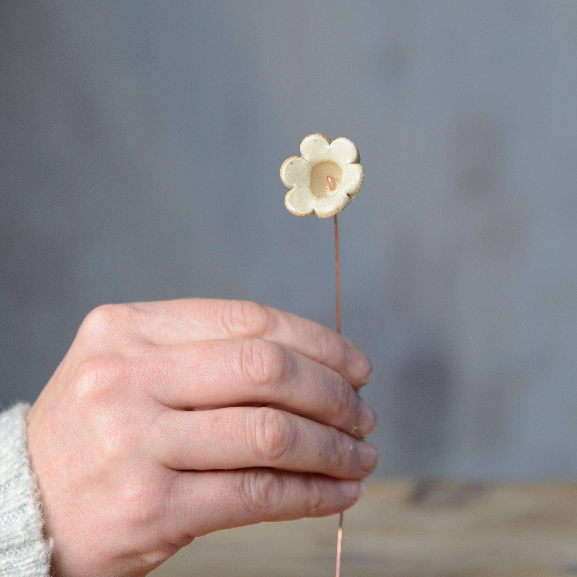 A hand holding a yellow ceramic flower bud stem on a copper wire