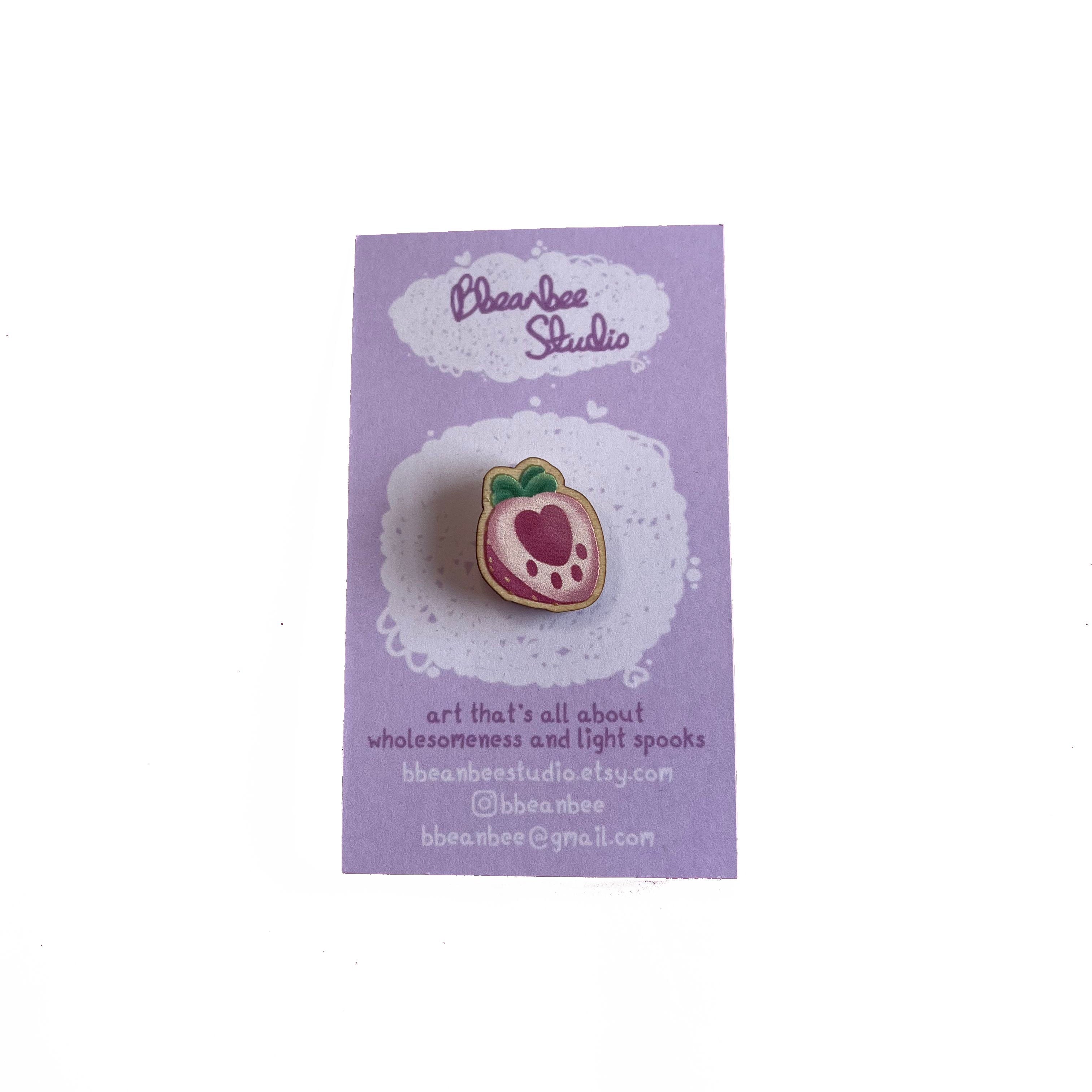 Mini wooden pin badge of a pink pawberry (heart-shaped strawberries with a paw shape inside). This badge is printed onto 3mm thick responsibly sourced European birch plywood.