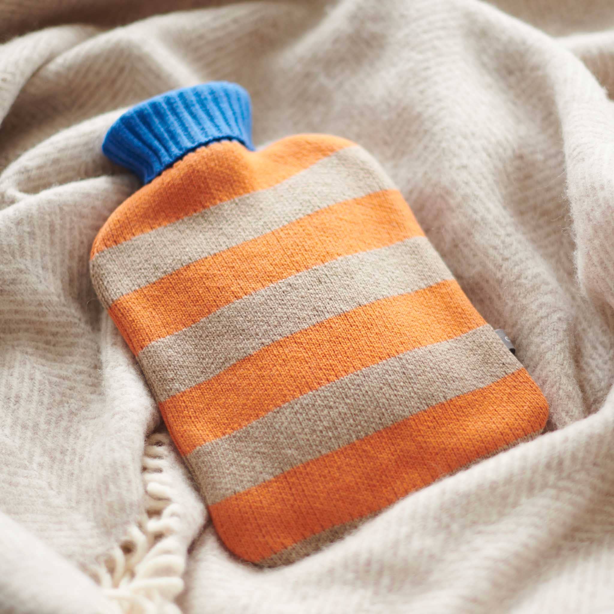 Striped hot water bottle with blue top on beige fabric.