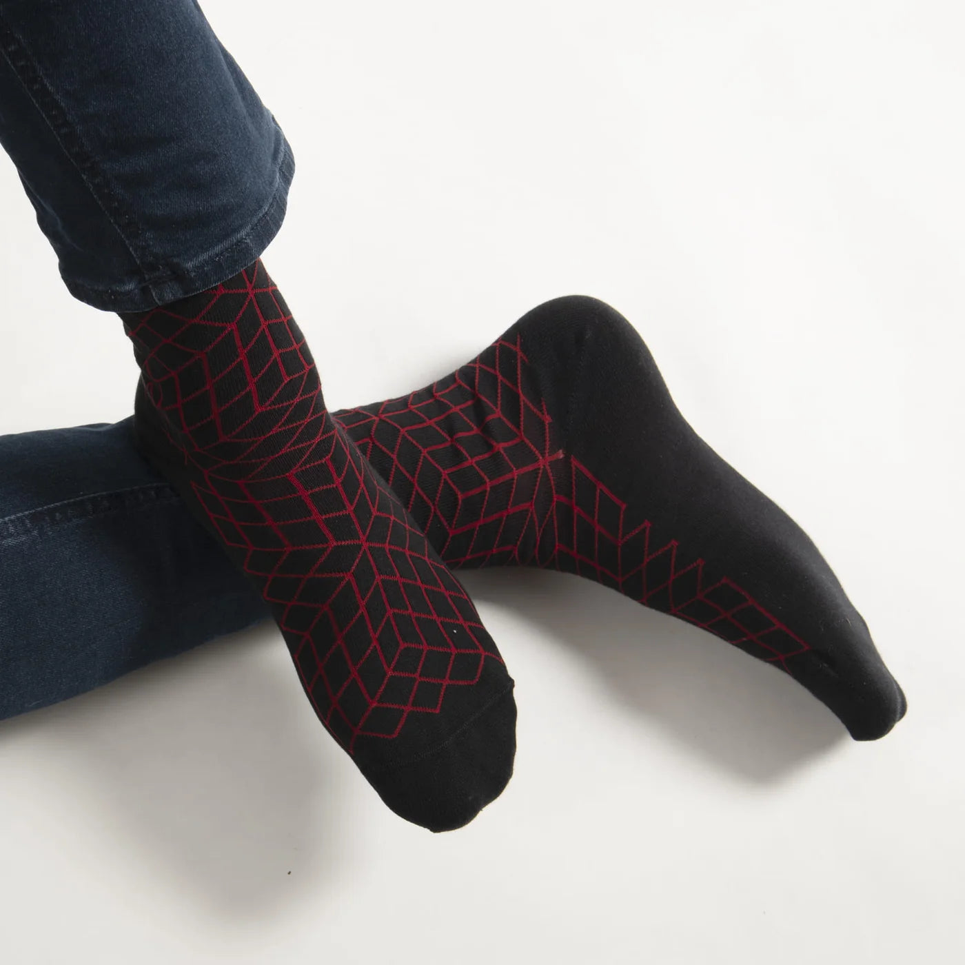 Black socks with red geometric pattern worn by a person with blue jeans on a white background.