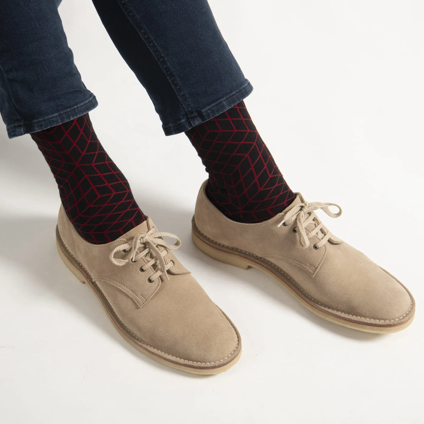 Beige shoes worn with dark jeans and red patterned socks on a white background.