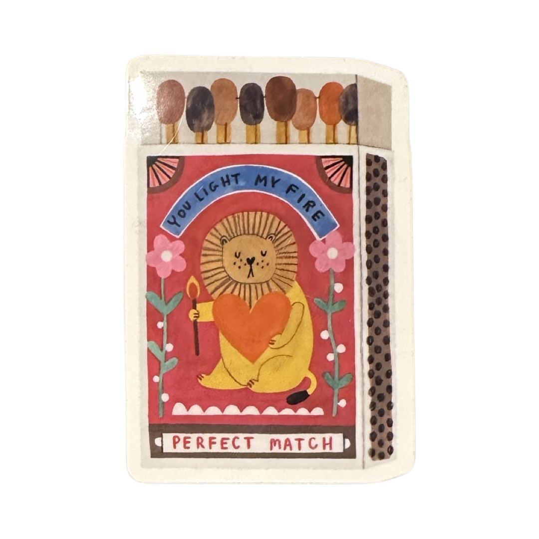 This vinyl sticker features an open box of matches with a cute lion carrying a red love heart and the text 'You light my fire, Perfect Match'.