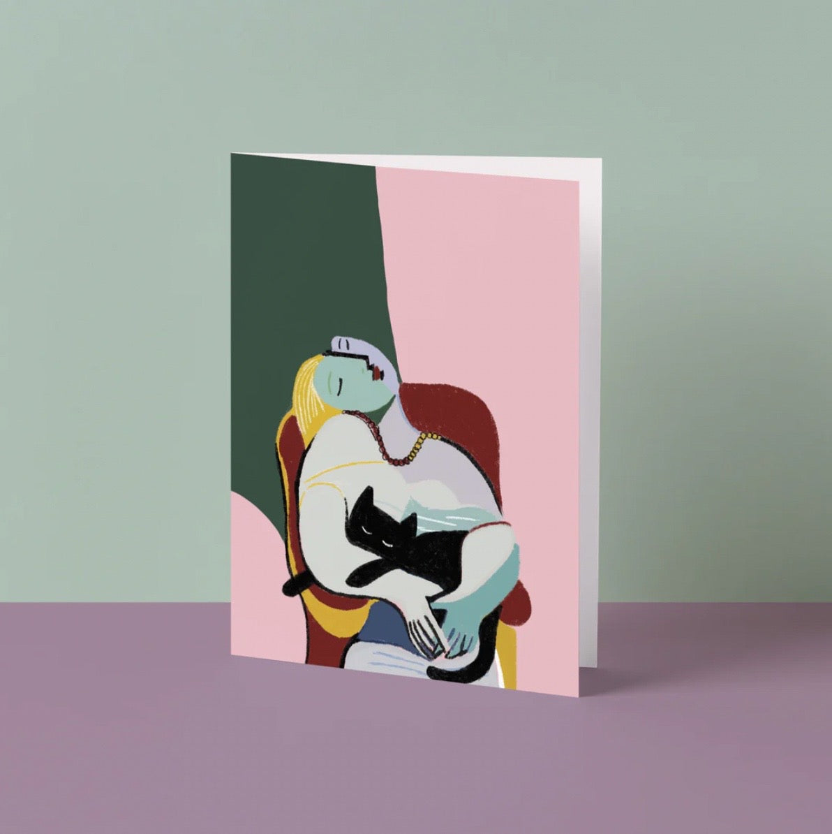 Greeting card with an illustration of a woman holding a black cat on a pink and green background.