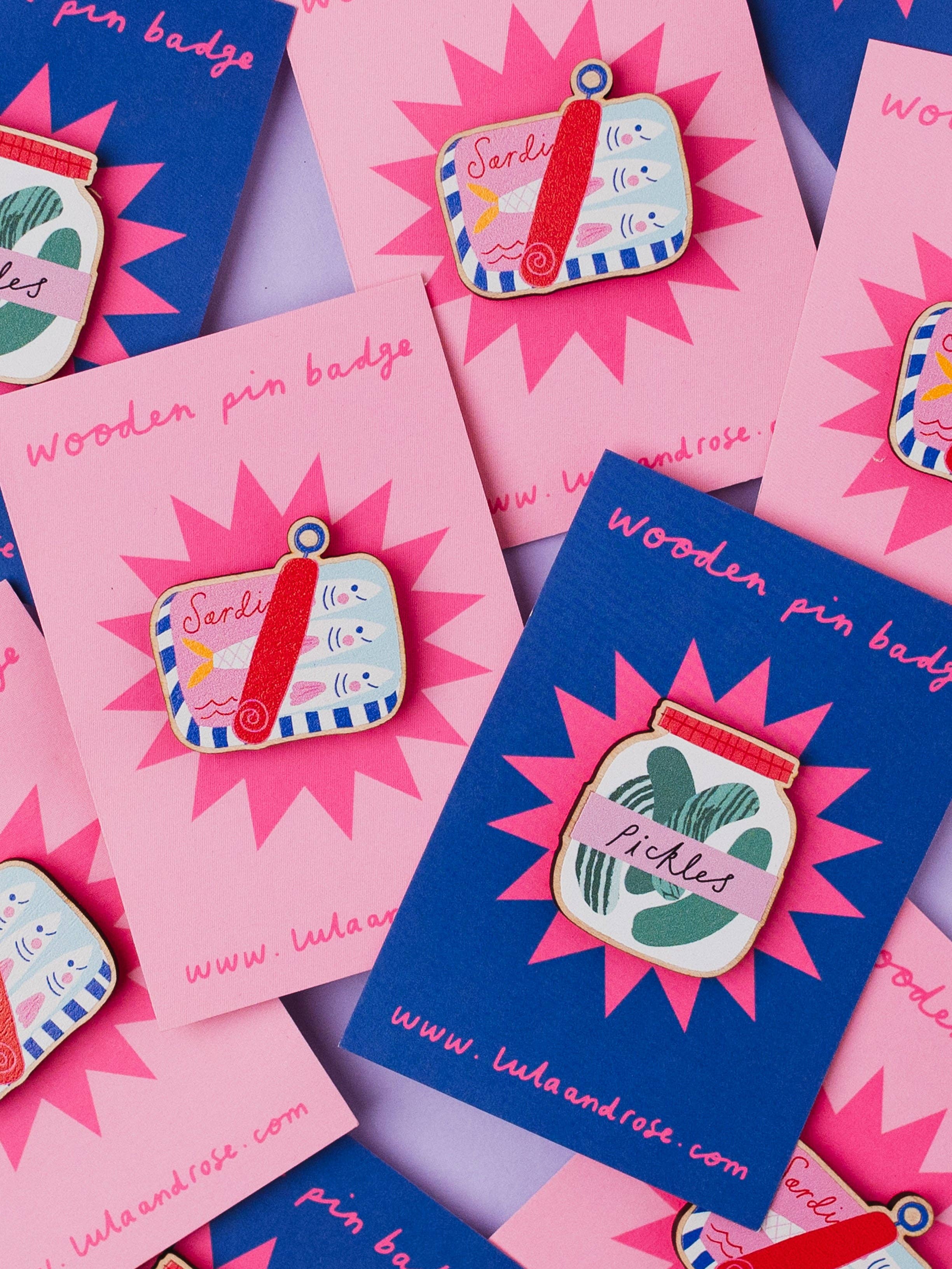 A pile of pin badges on pink and blue backing card.