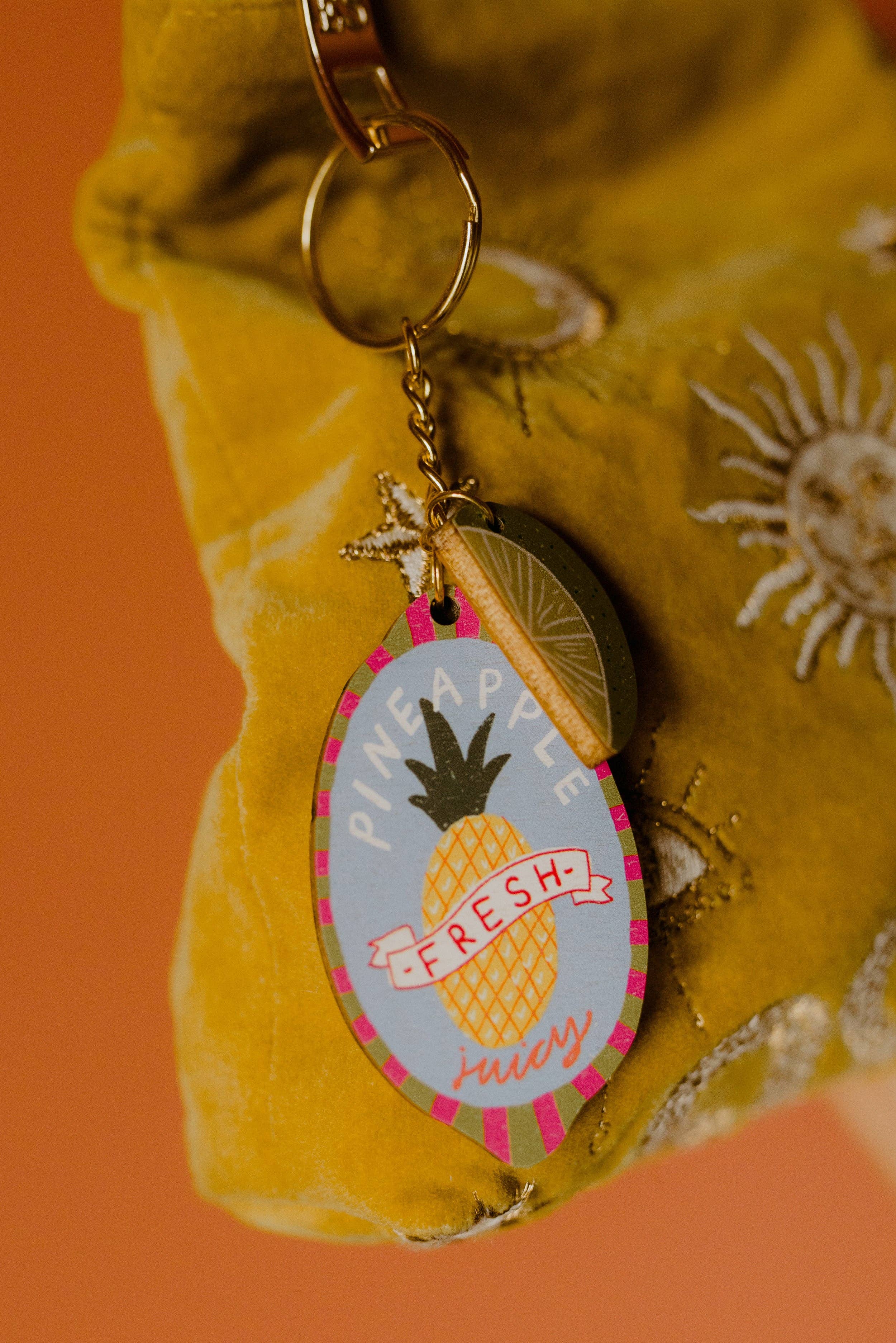 Pineapple-themed keychain on a yellow textured fabric background.