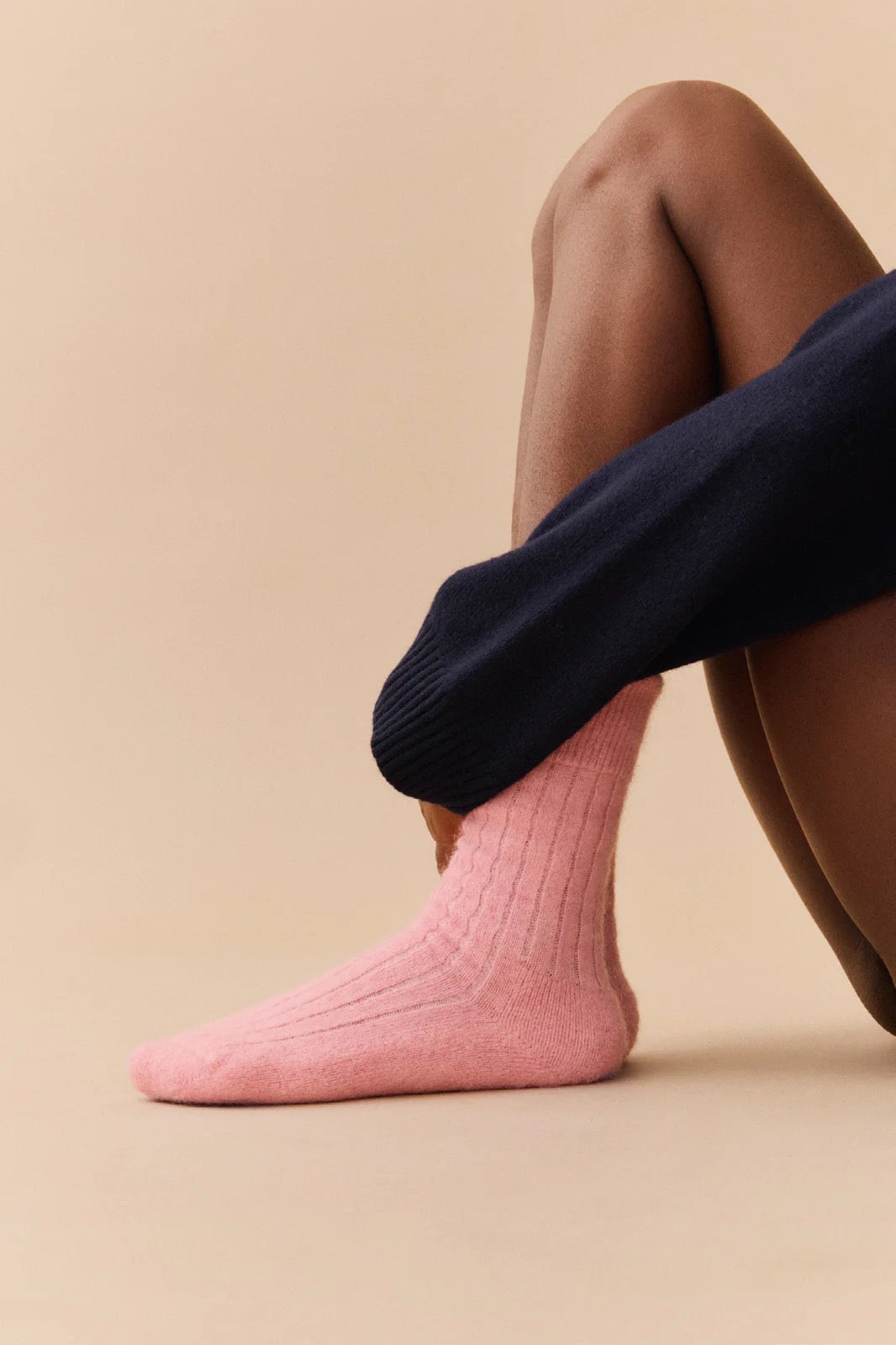 Person wearing pink socks and a navy jumper on a beige background.