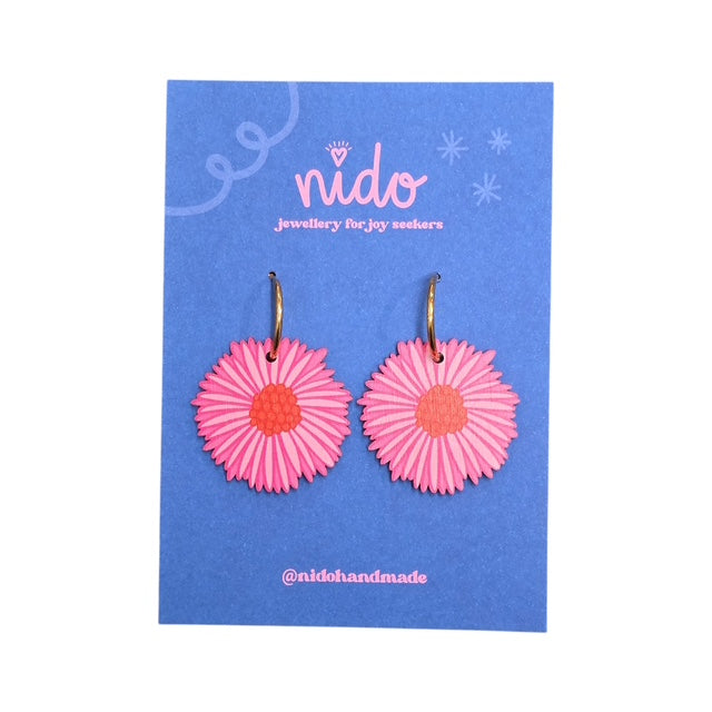 These wooden blossom-shaped earrings feature pink petals with a red centre presented on a blue backing card