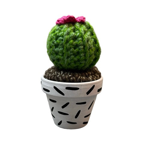 Handmade round crochet cactus with pink flowers in a white and black speckled terracotta pot.