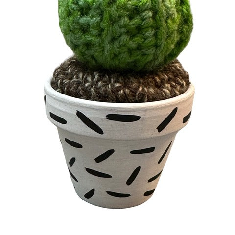 Handmade round crochet cactus with pink flowers in a white and black speckled terracotta pot.