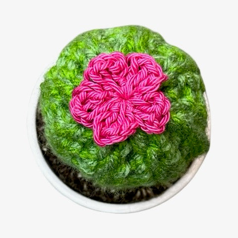Handmade round crochet cactus with pink flowers in a white and black speckled terracotta pot.
