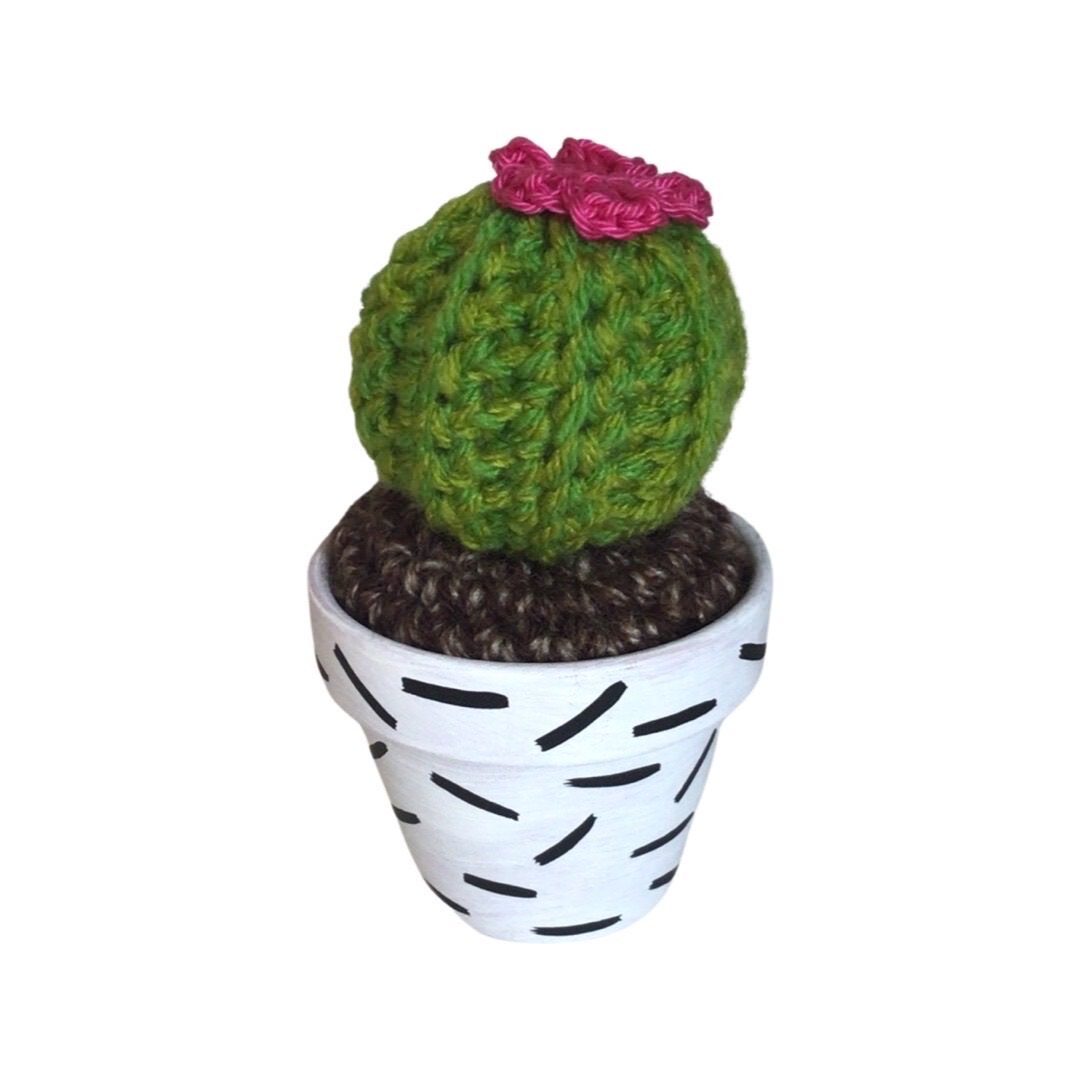 Handmade round crochet cactus with pink flowers in a white and black speckled terracotta pot.