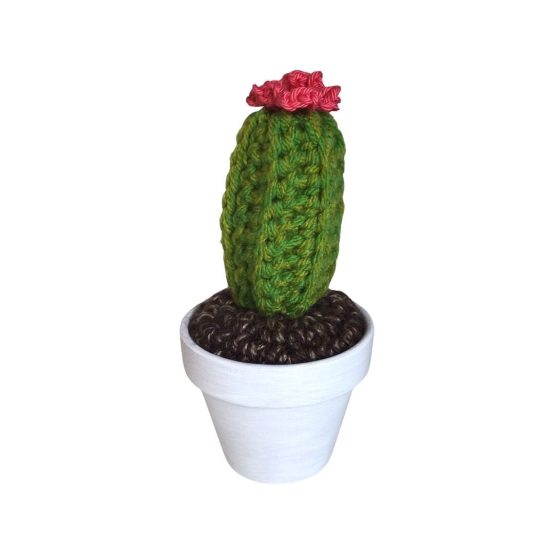 Handmade tall crochet cactus with a pink flower in a white painted terracotta pot. 