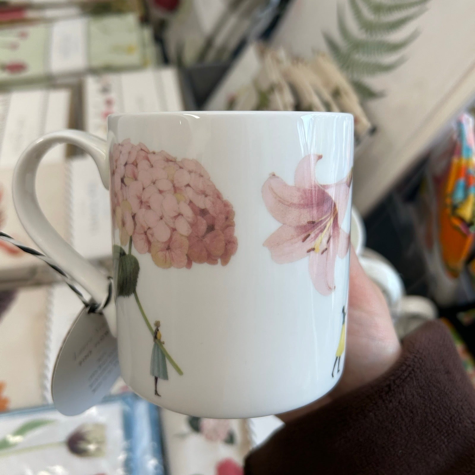 White mug with floral design held in a hand against a blurred background.