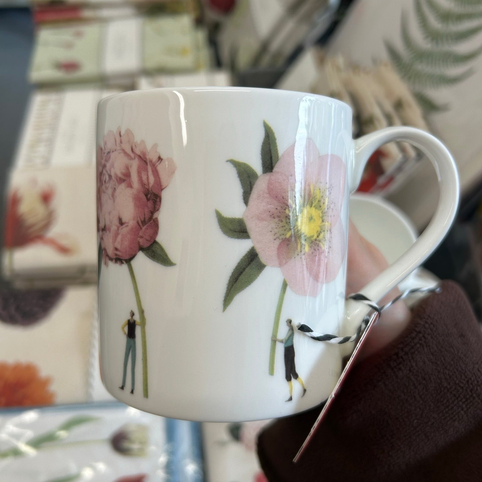 White mug with floral design held by a person, with a blurred background.