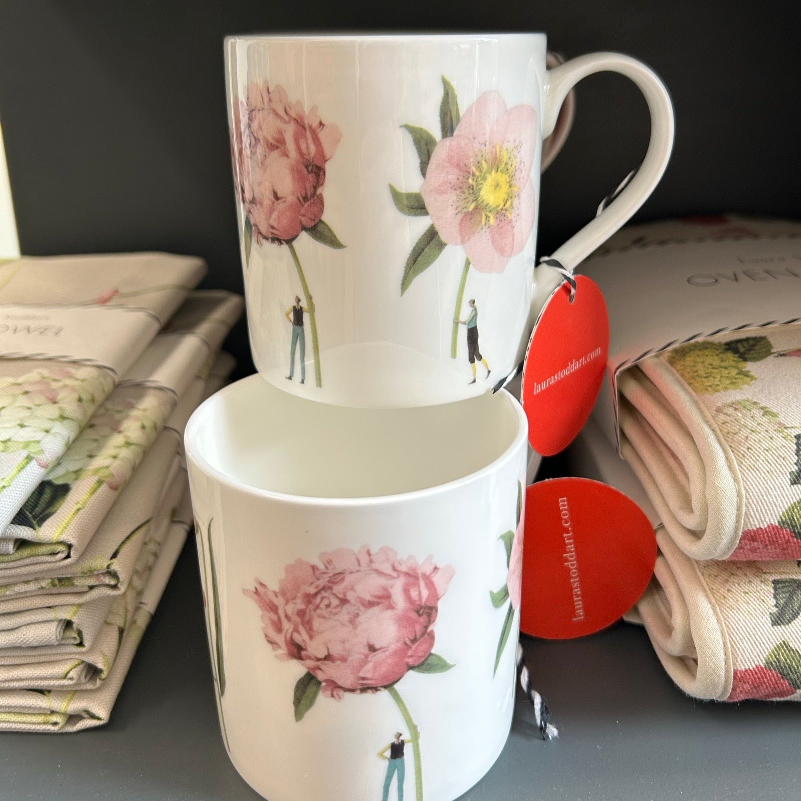 Two floral ceramic mugs piled on top of each other on a dark grey shelf.