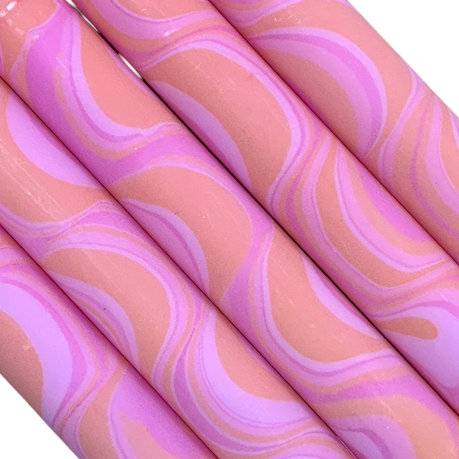 A row of 5 handmade dinner candles marbled in shades of pink and orange.