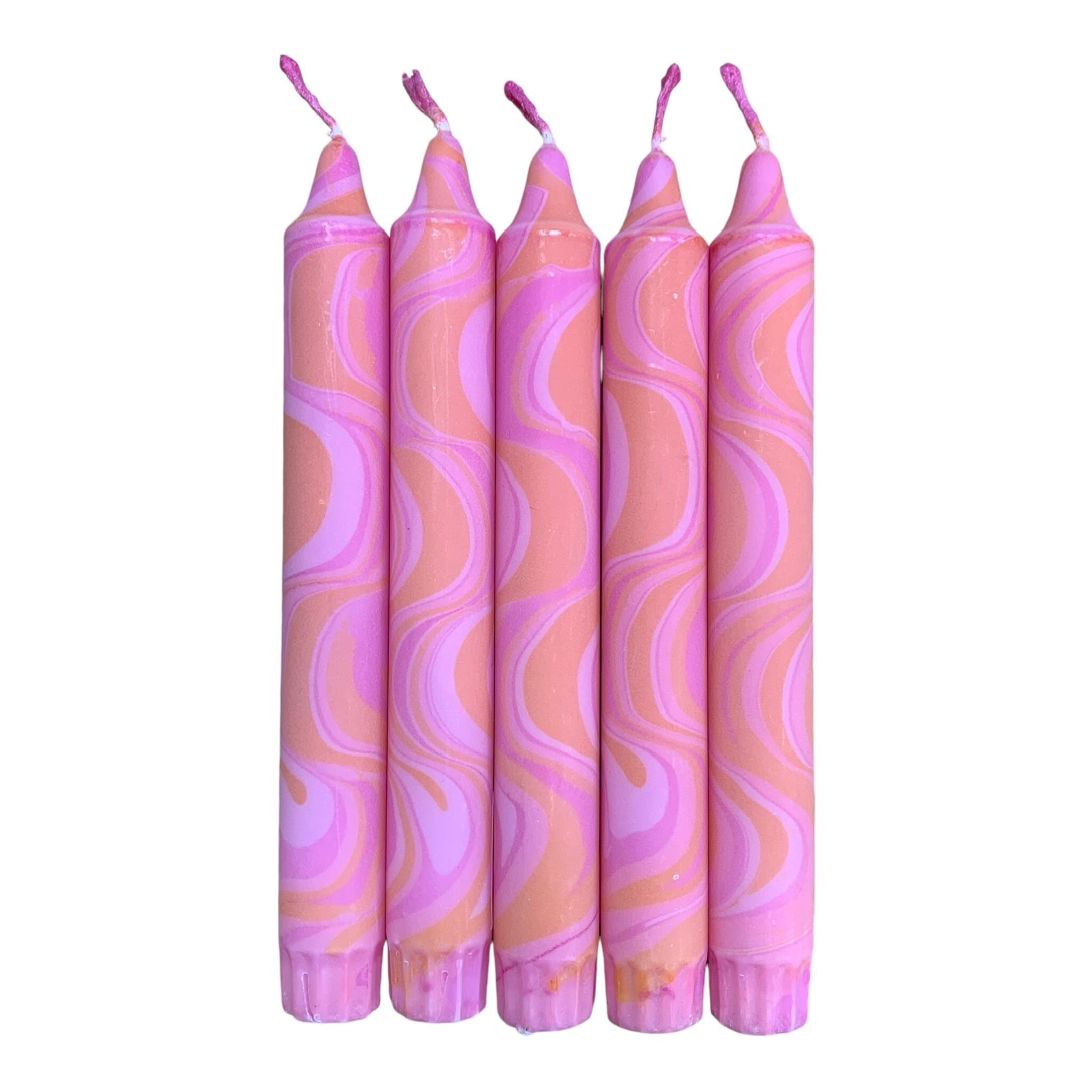 A row of 5 handmade dinner candles marbled in shades of pink and orange.